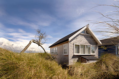 Mudeford beach hut against cloudy blue sky with long grass in foreground