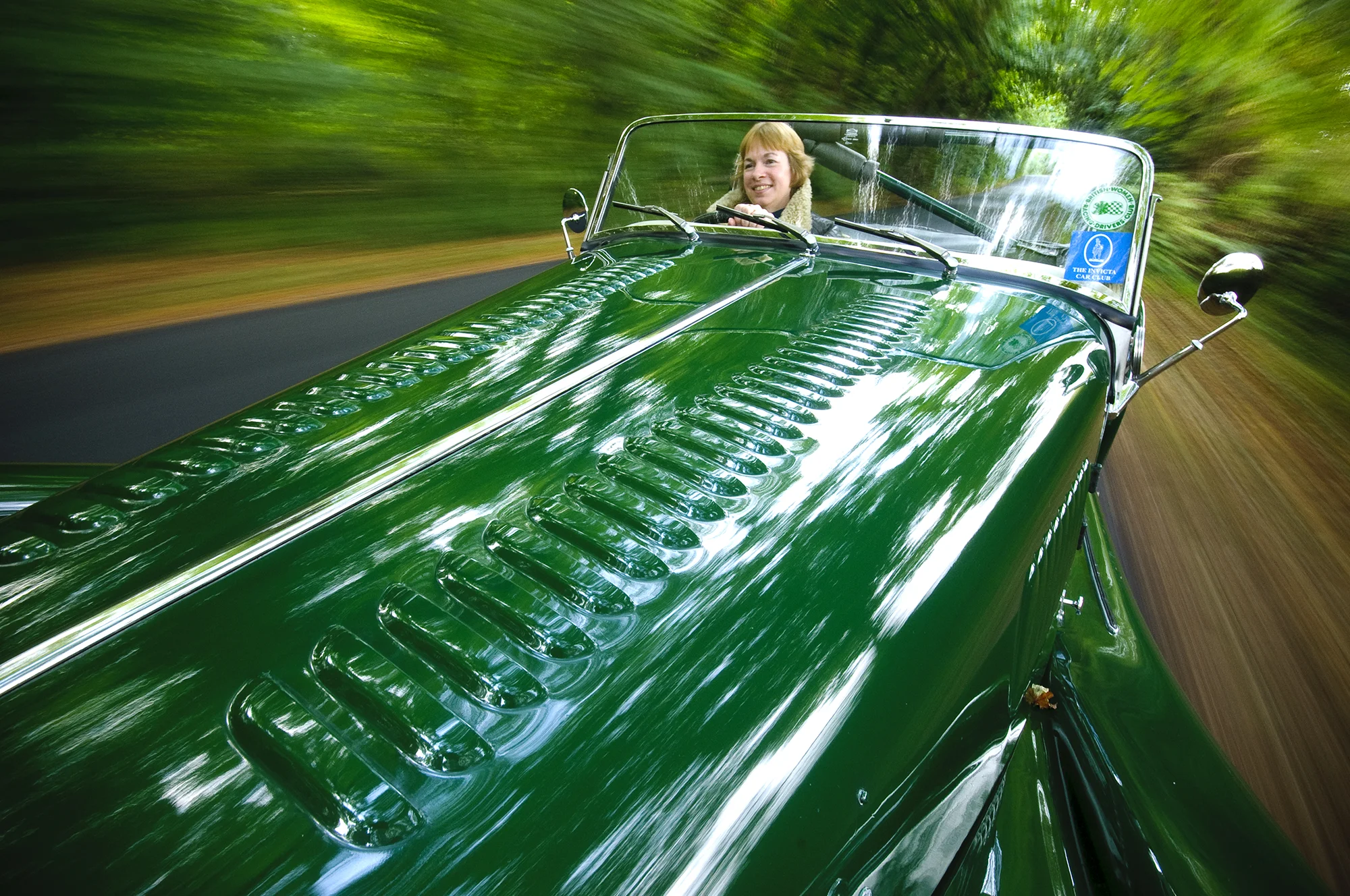 woman in fast moving green vintage car with hedges blurring past