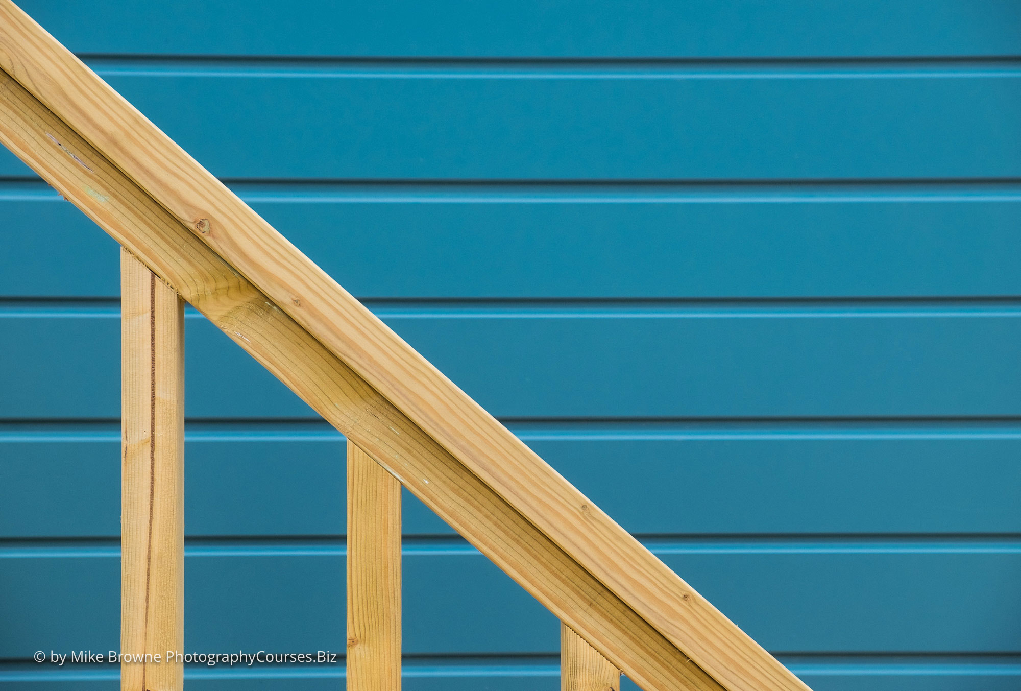 Contrasting brown hand rail in front of blue horizontal panelling of beach hut