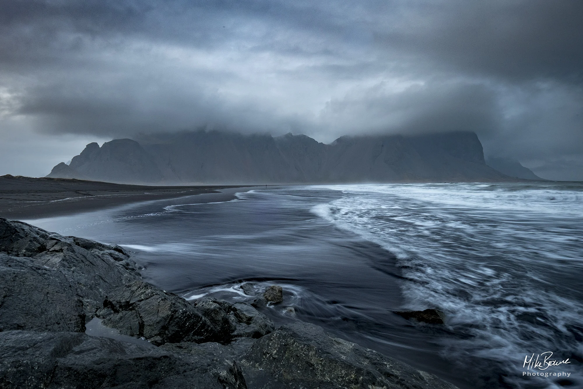 Foreground rocks and wet black sand beach leading to mountain at Westrahorn in Iceland