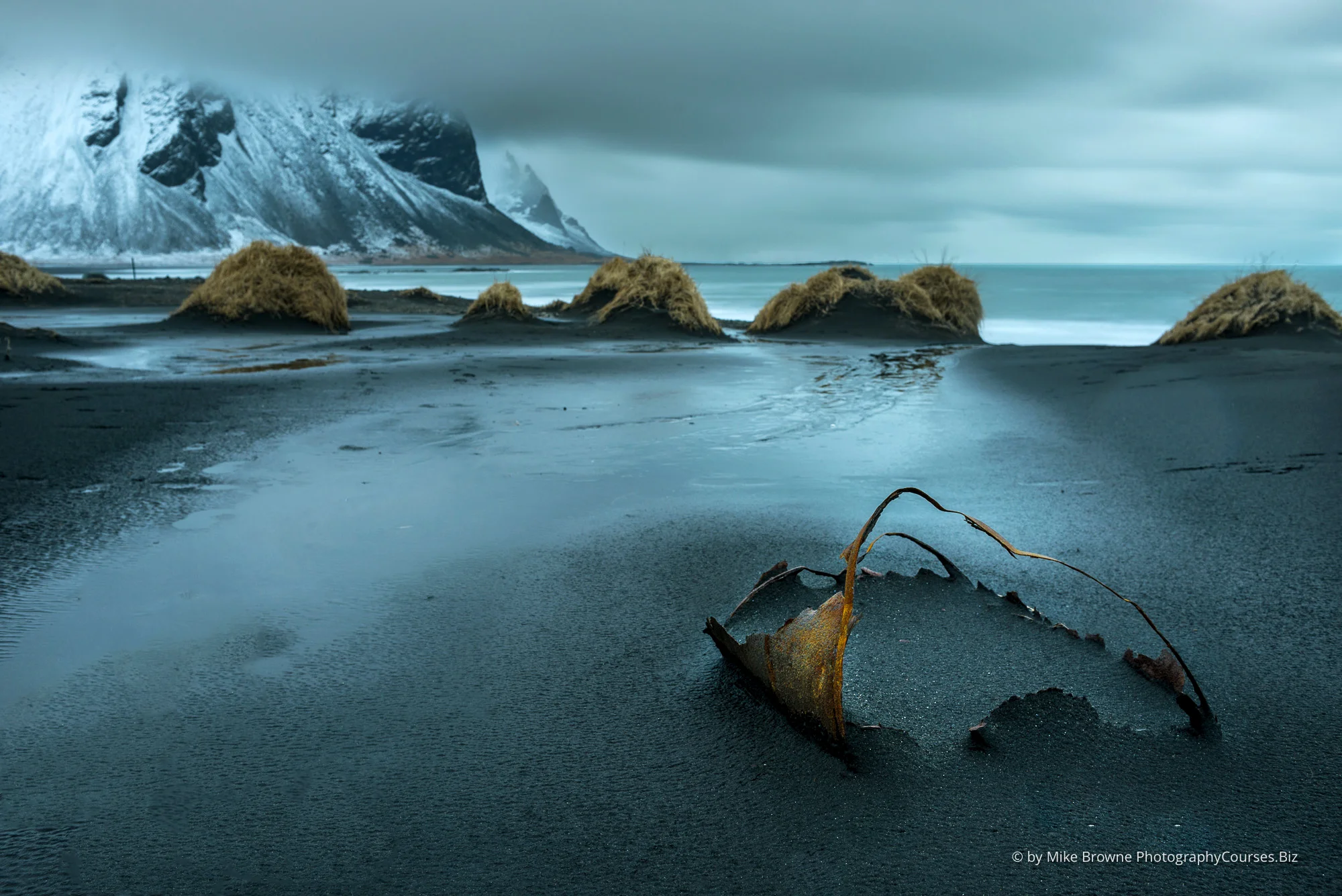 Rusting skeleton of an oil drum in black sand dunes and snow covered mountain at Westrahorn in Iceland