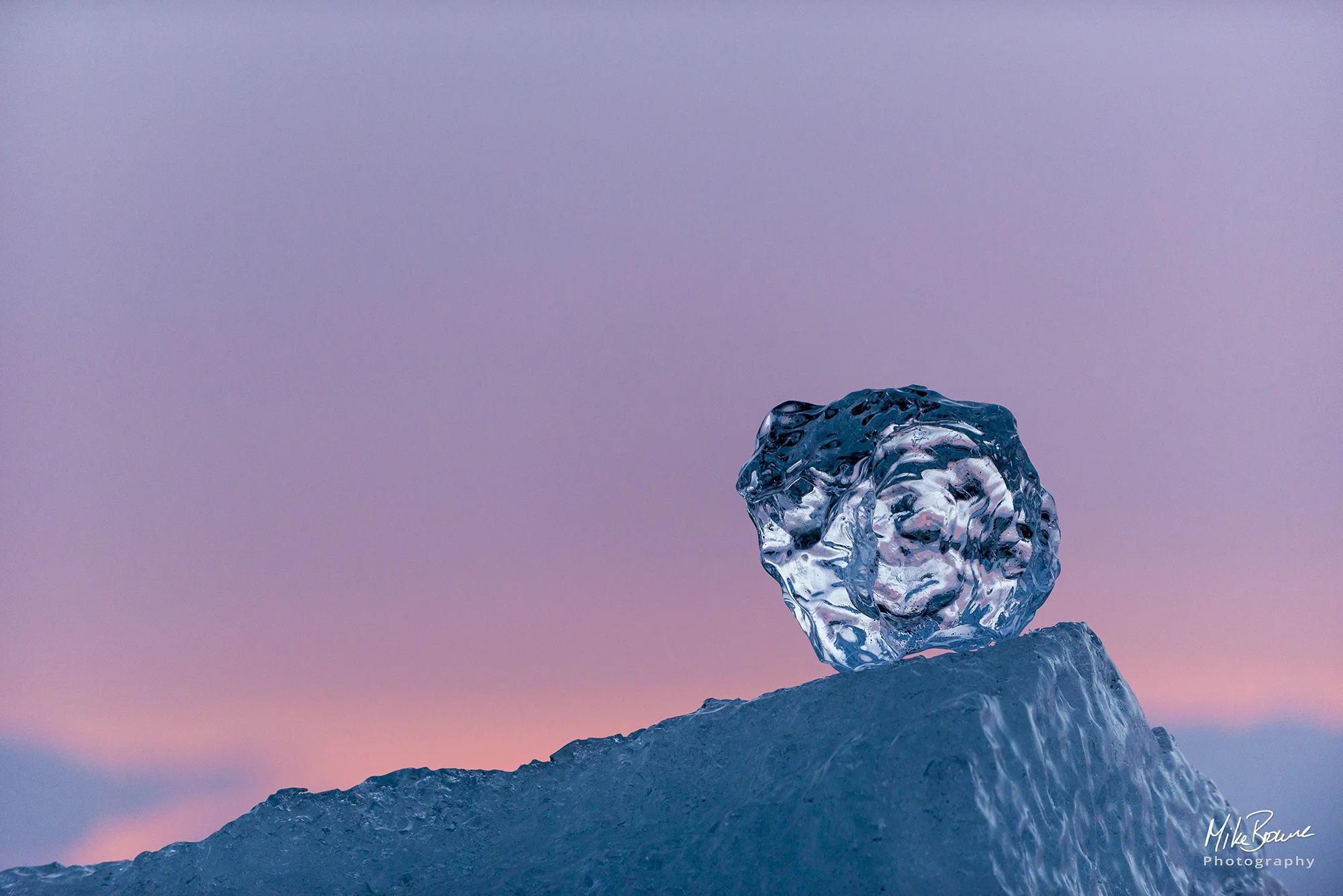 Crystal iceberg balancing on blue iceberg against sunset sky