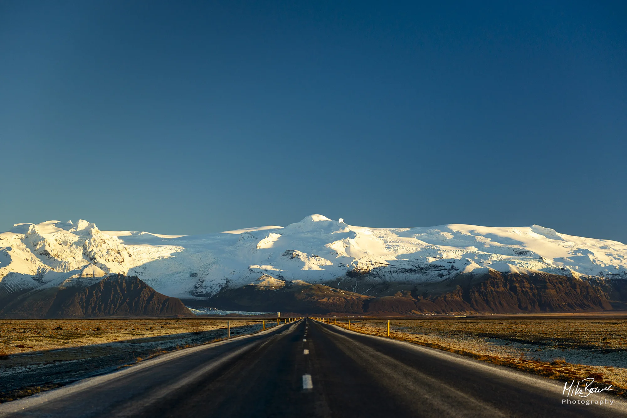 Road leading to snow covered mountains and blue sky in south Iceland