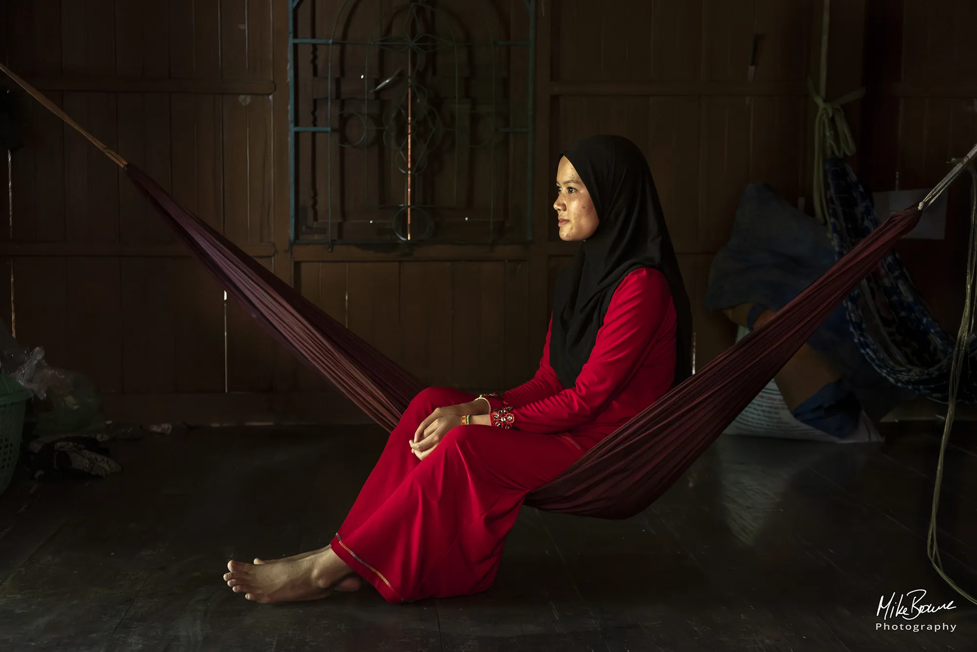 Muslim woman in red sitting on a hammock in a wooden room
