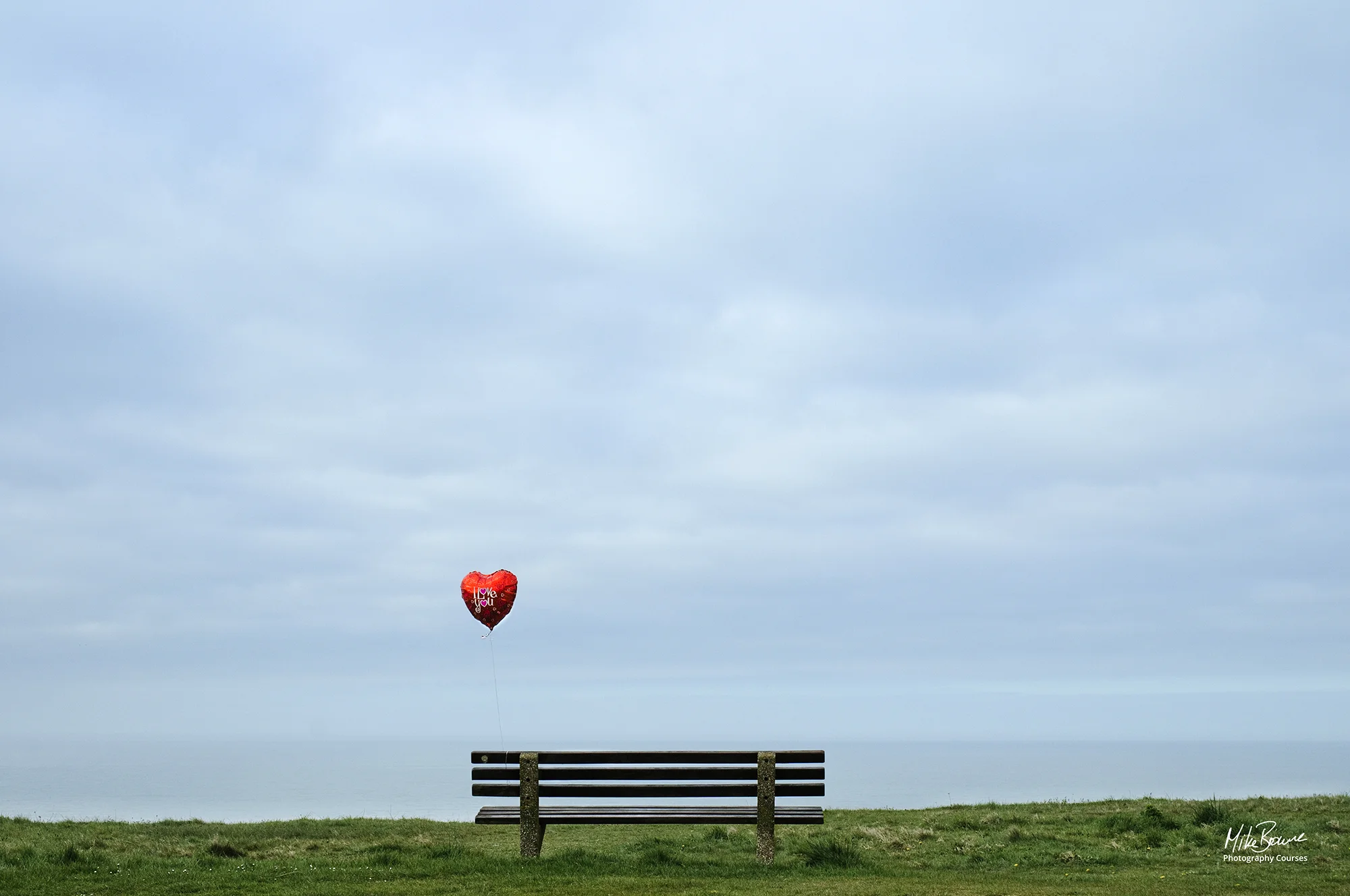 Red balloon tied to end of a bench against grey sky