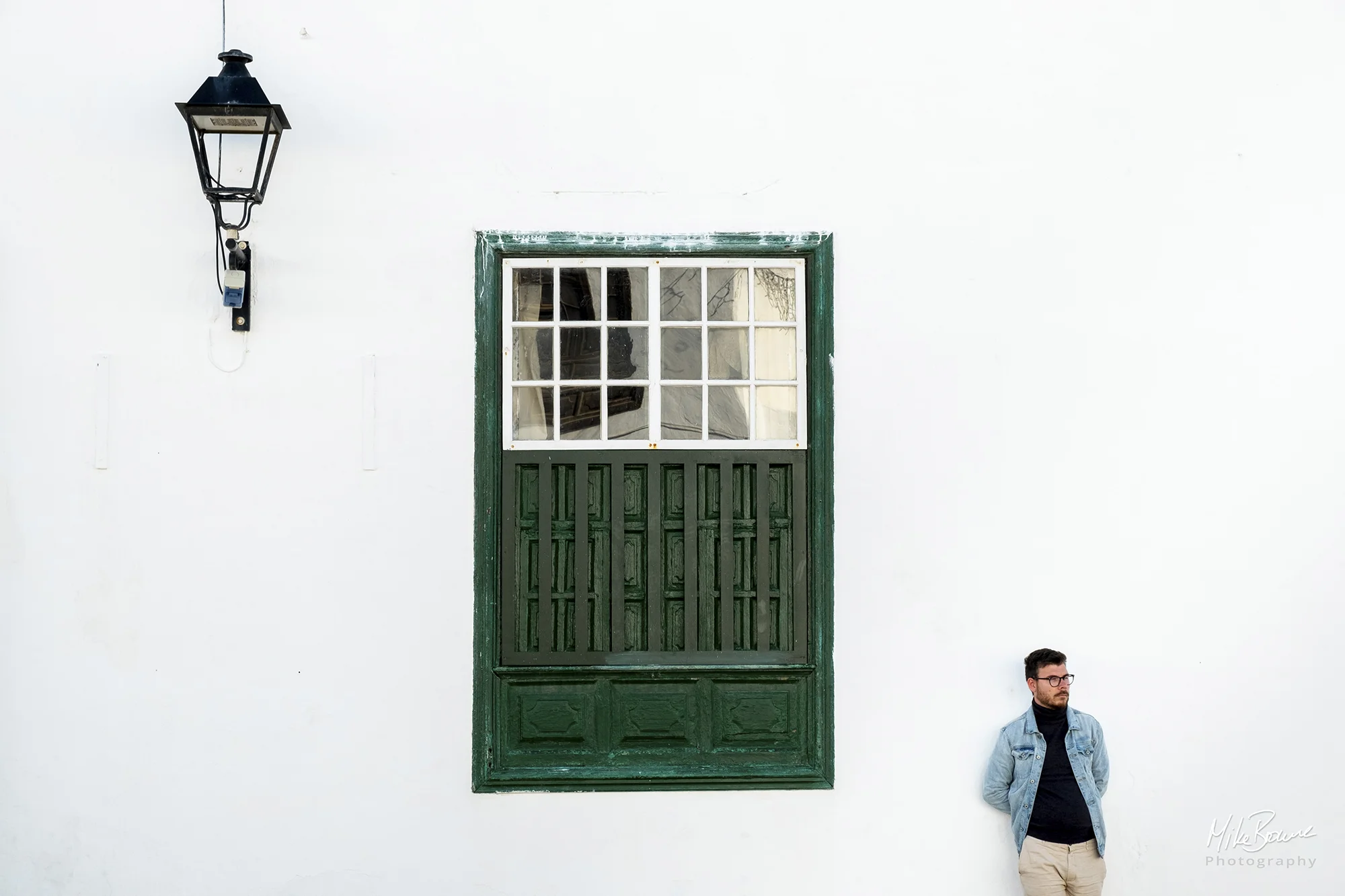 Man leaning against a white wall with large green door and ornate street lamp in Teguise, Lanzarote