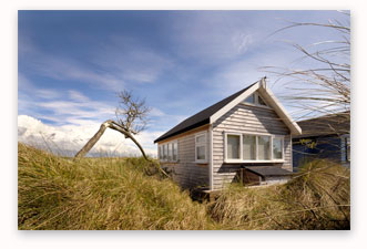 Smaller version of Mudeford beach hut against cloudy blue sky with long grass in foreground