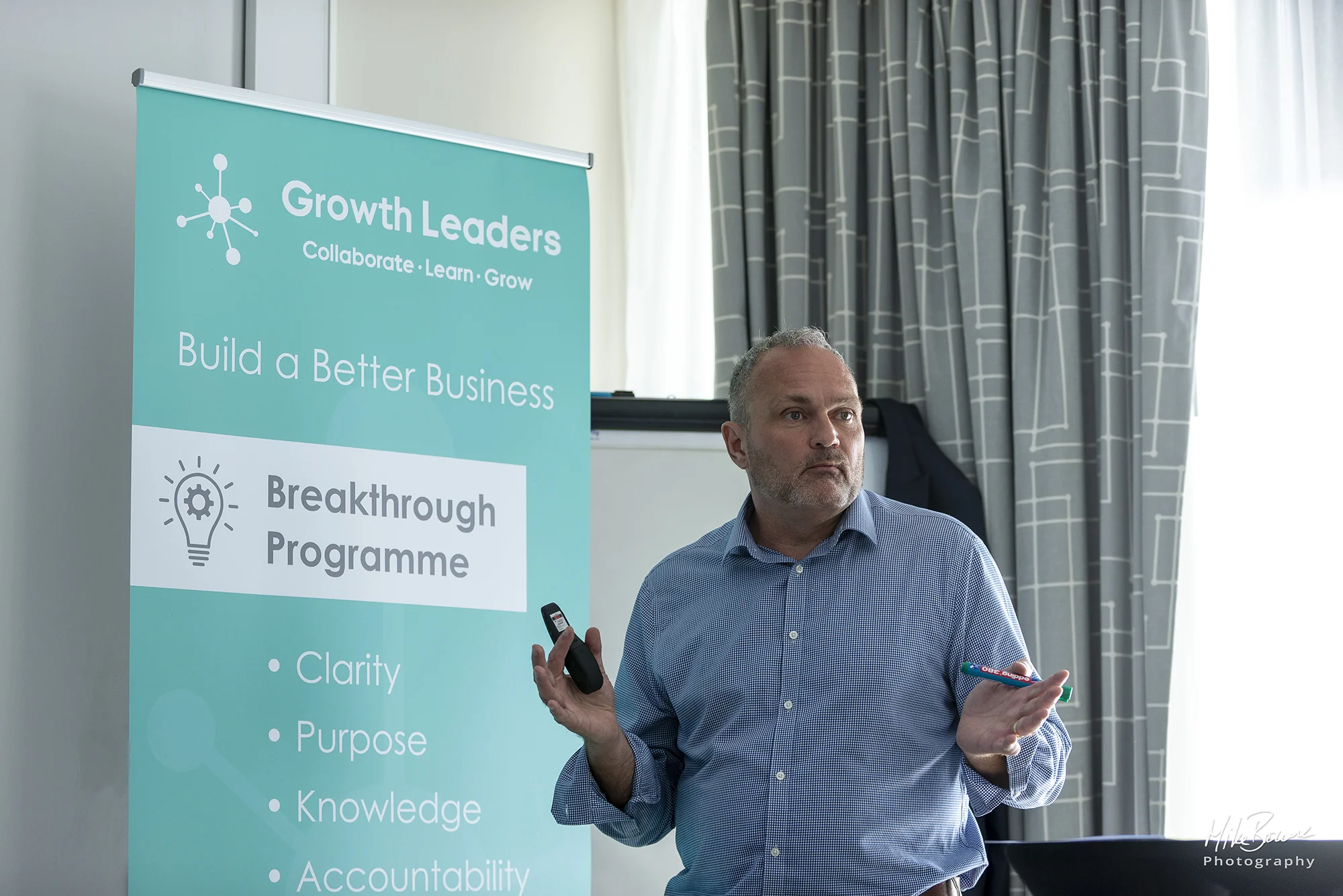 Man doing a business presentation in front of a turquoise and corporate Growth Leaders sign