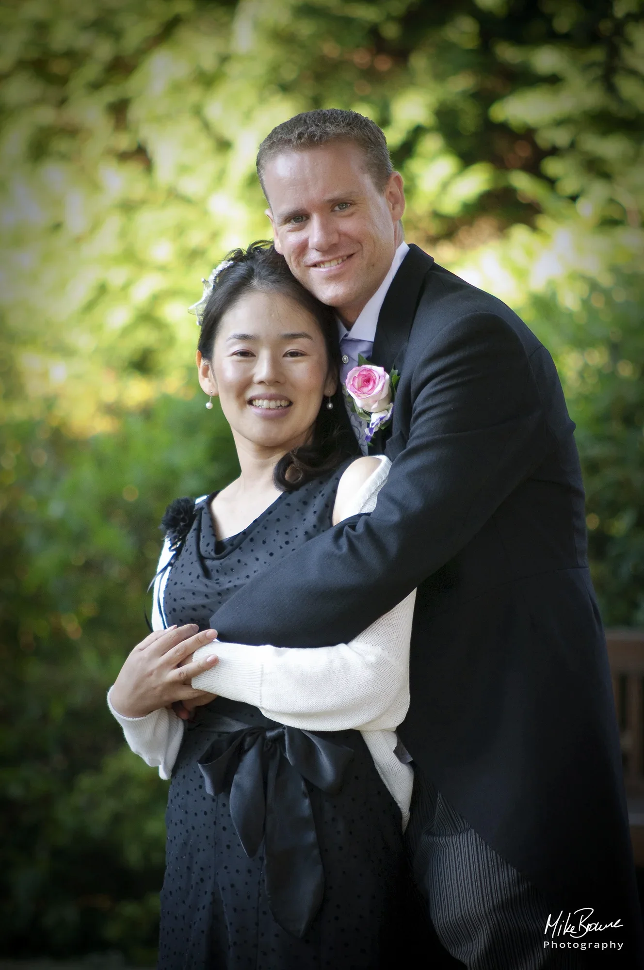 Bride and groom with pink button hole embracing in a garden