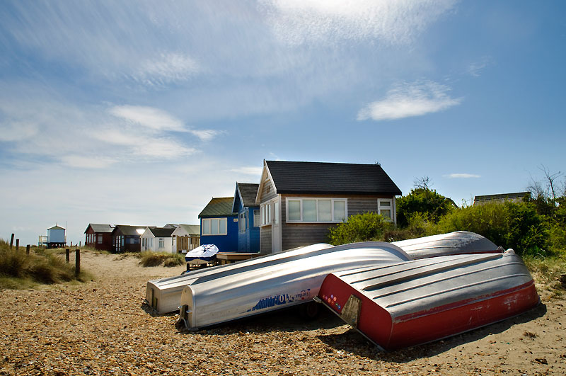 four upturned skiffs laying on sand with beach huts in the background