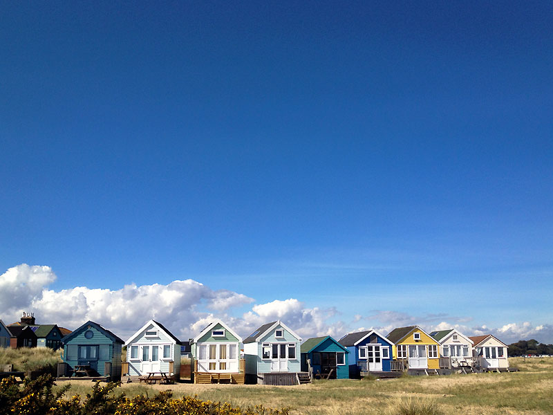 Nine beach huts at Hengistbury Head with clear blue sky and cumulus low clouds