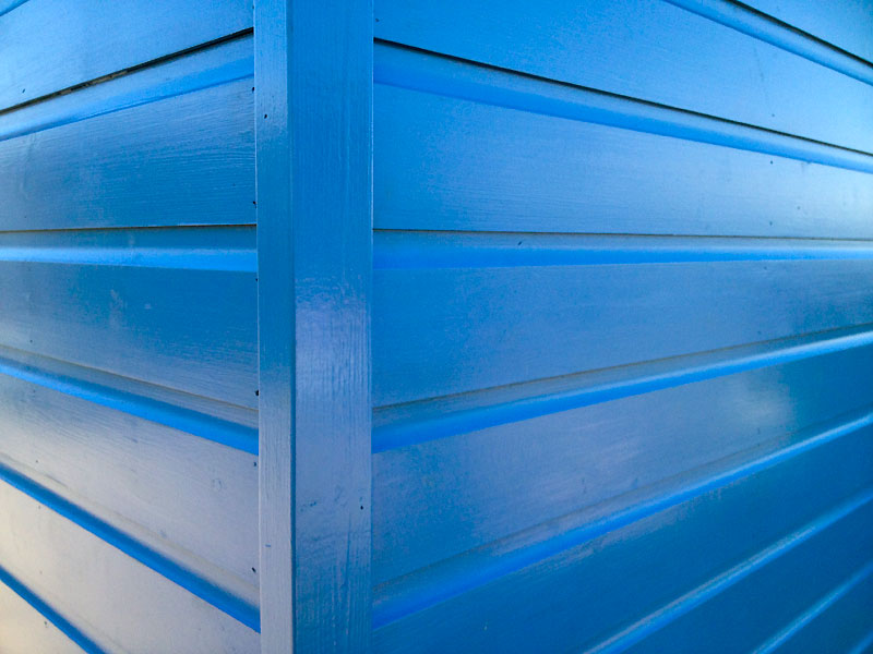 Corner shot of a bright blue freshly painted beach hut with horizontal panels