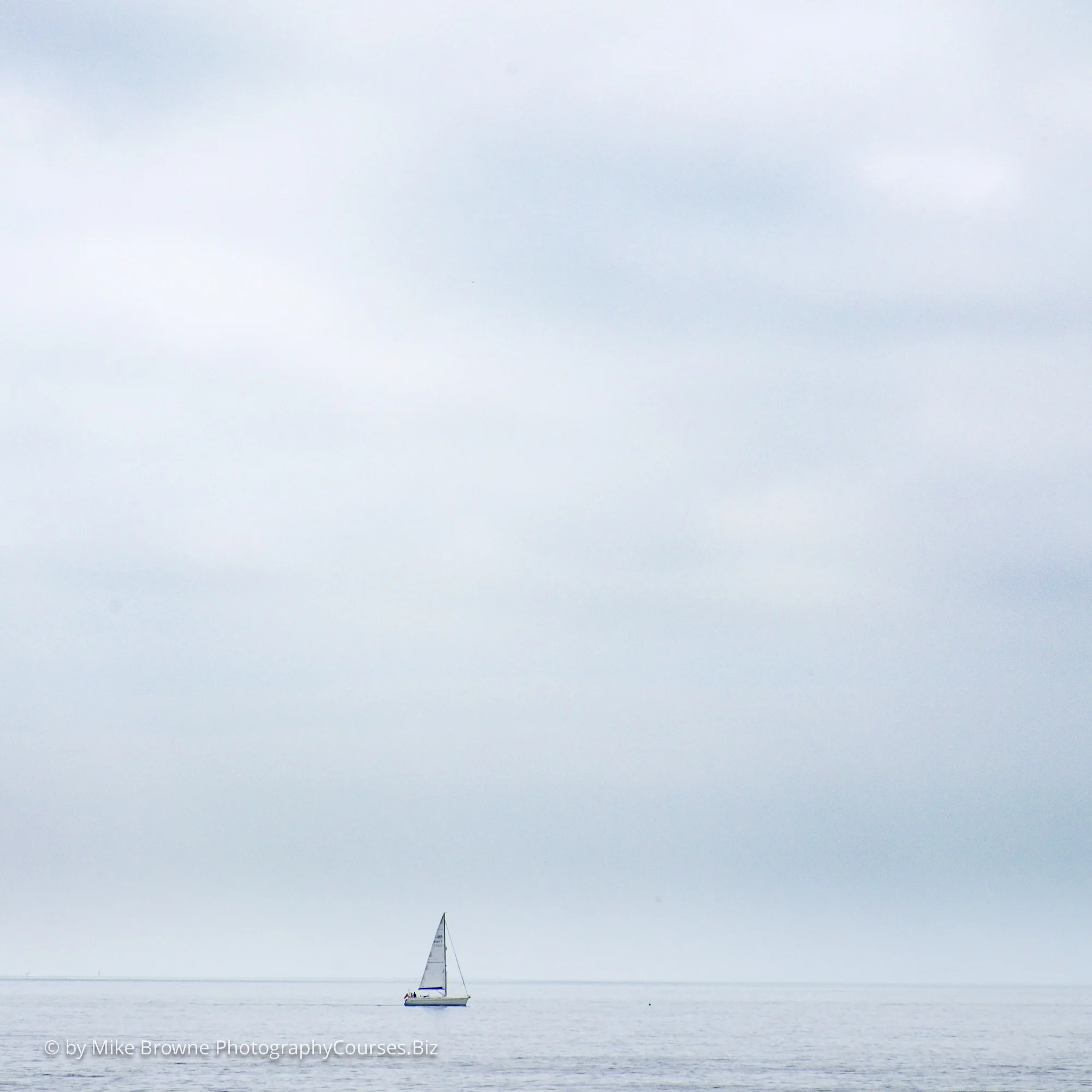 Sailboat small in the distance on a clam sea with gentle clouds overhead