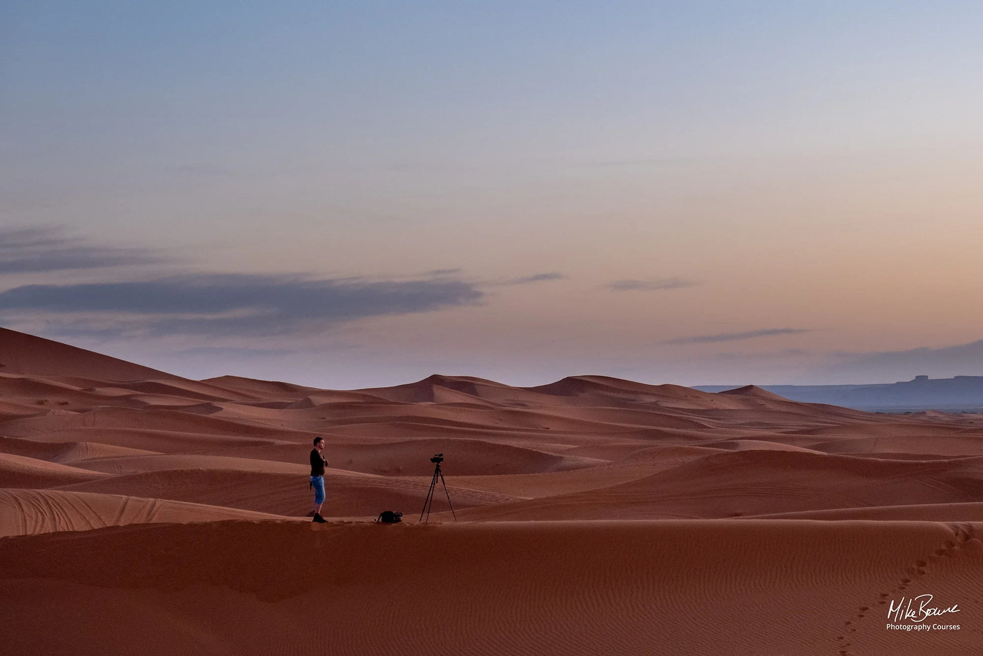 Man with a camera and tripod standing in the sand dunes at Merzouga in Morocco