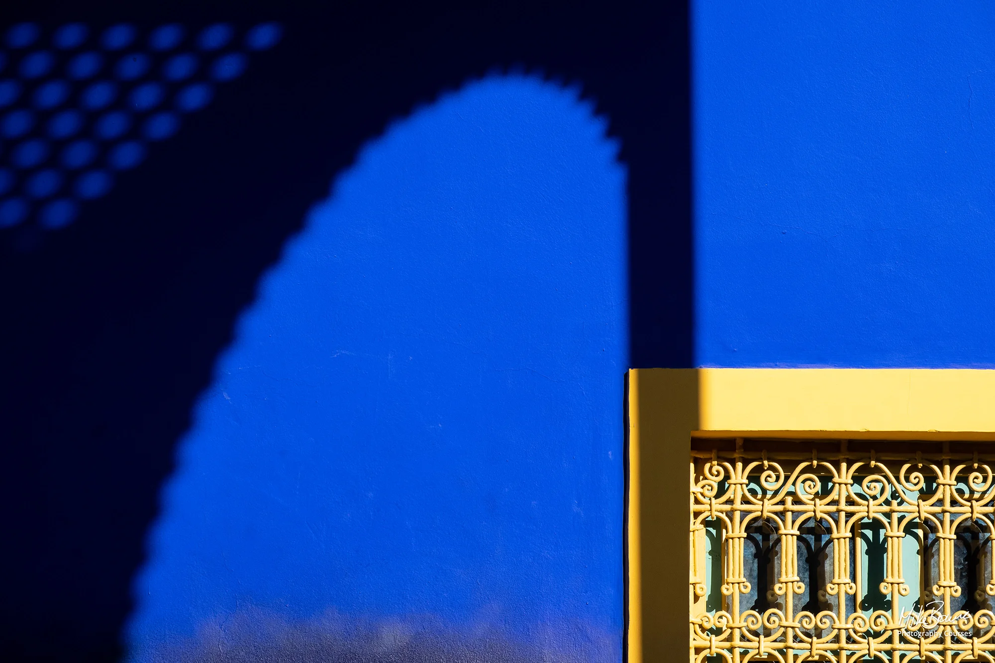 Curving ornate shadow on a blue wall with a golden doorway in Marrakech, Morocco