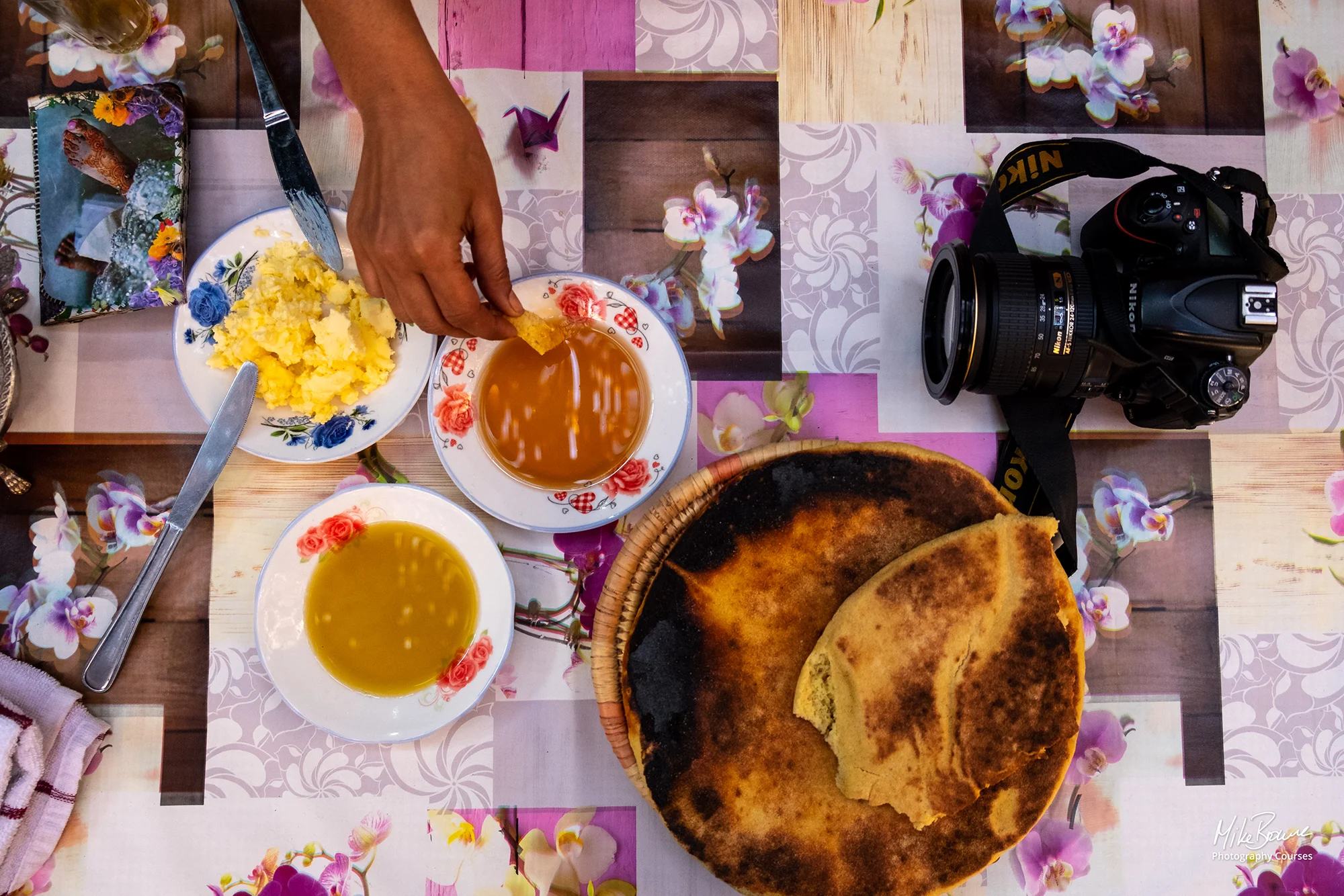 Hand dipping unleavened bread into a bowl of honey and a camera on table