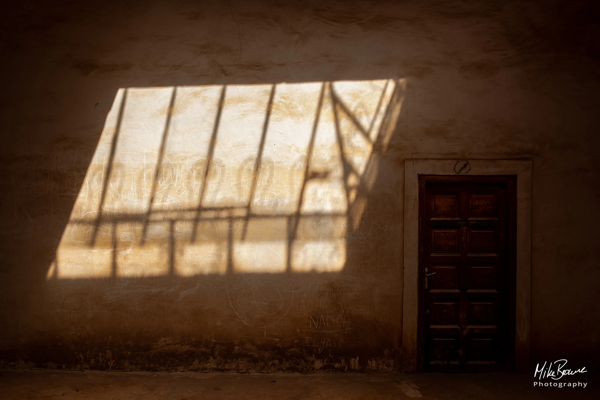 Highlight shape of a window on a shadowed graffiti wall and a green door nearby at a Kasbah in Morocco