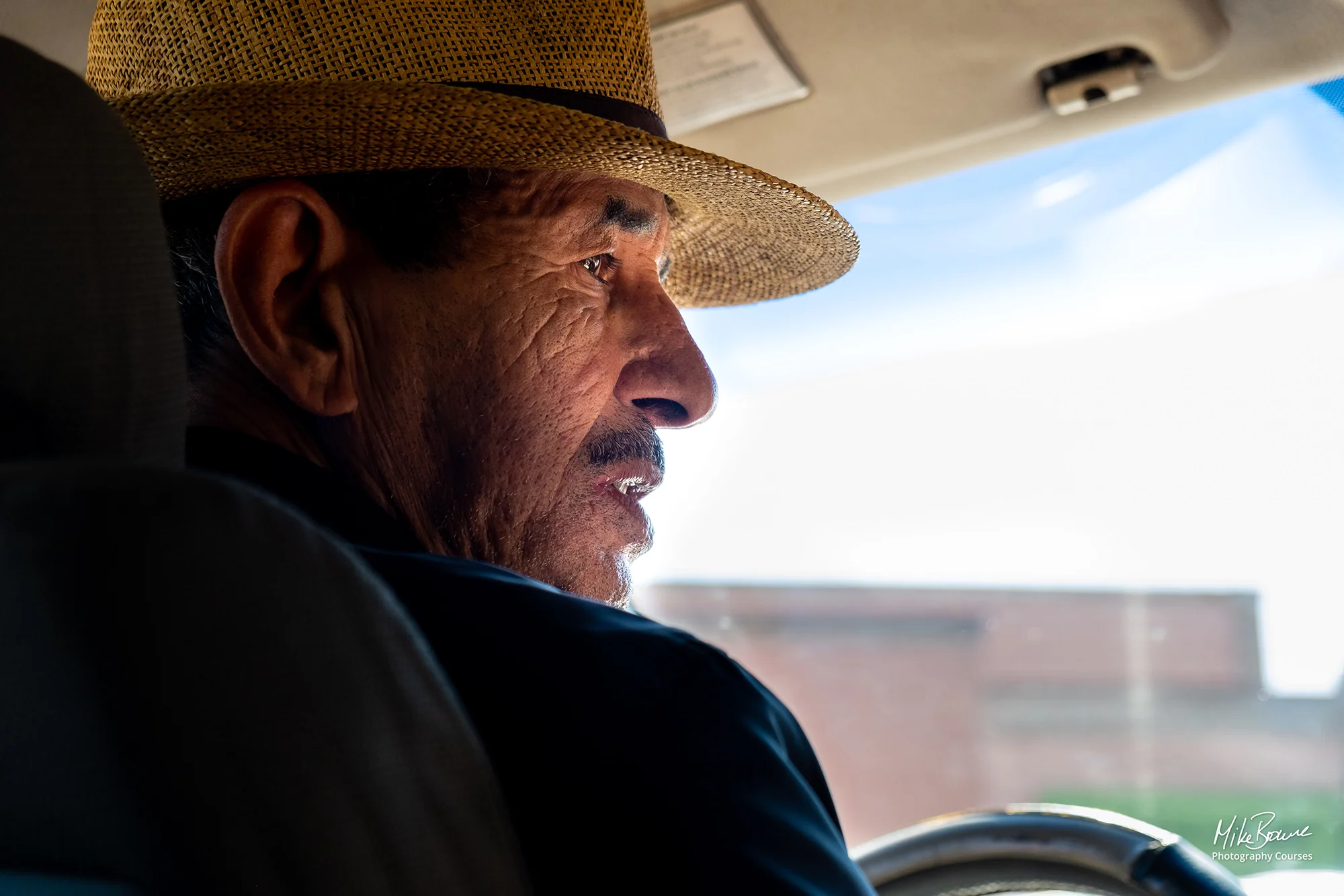 Man with a lined face wearing a straw hat at the wheel of a car in Marrakech, Morocco