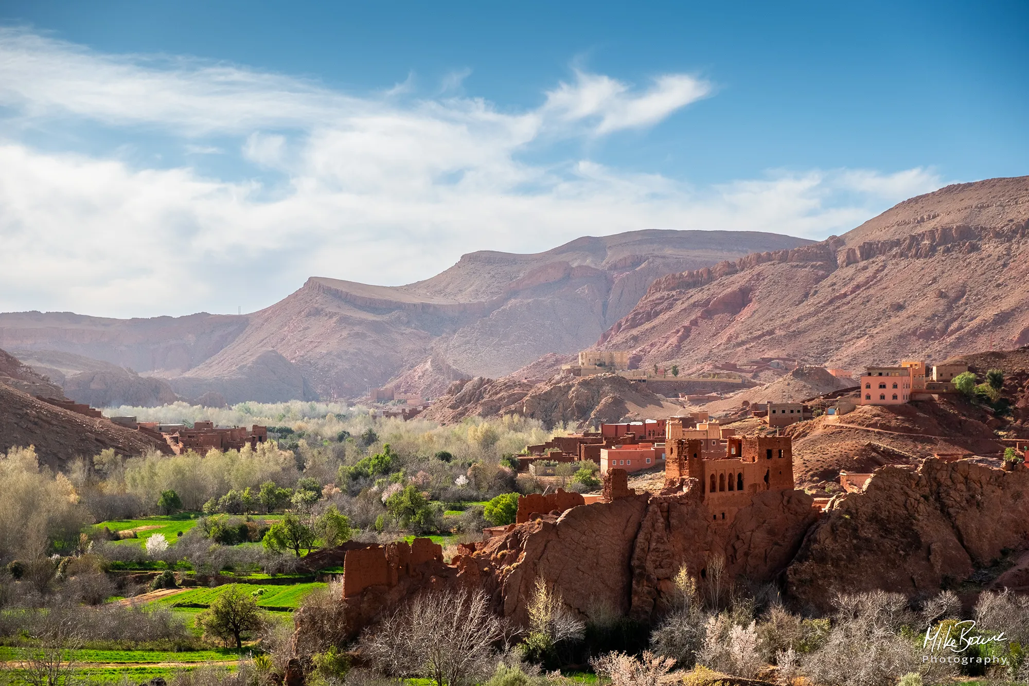 Green valley with a rustic red building on outcrop of rock in Todra Gorge Morocco