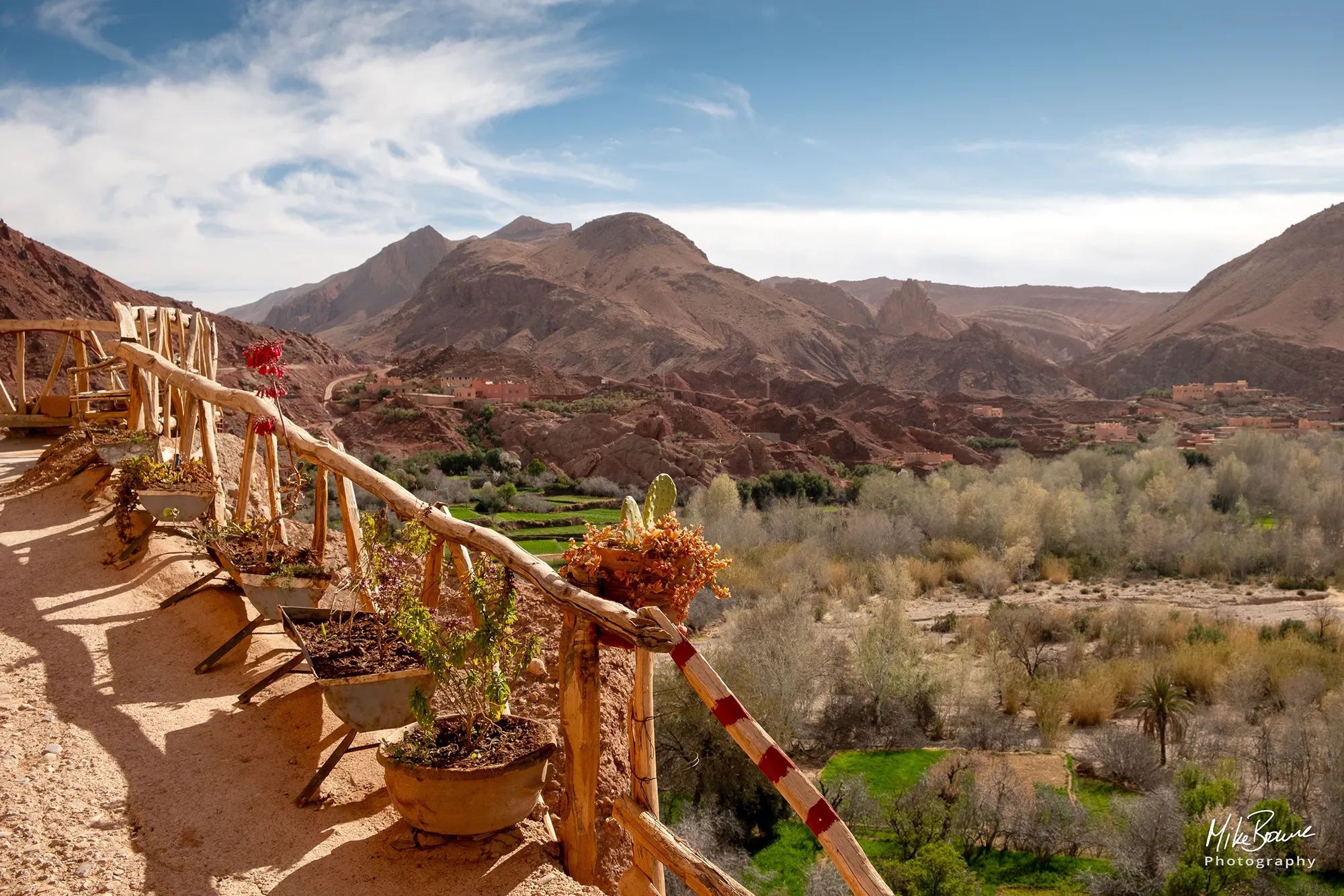 Footpath with rustic handrail Above a lush green valley with misty hills in background in the Dades Valley, Morocco