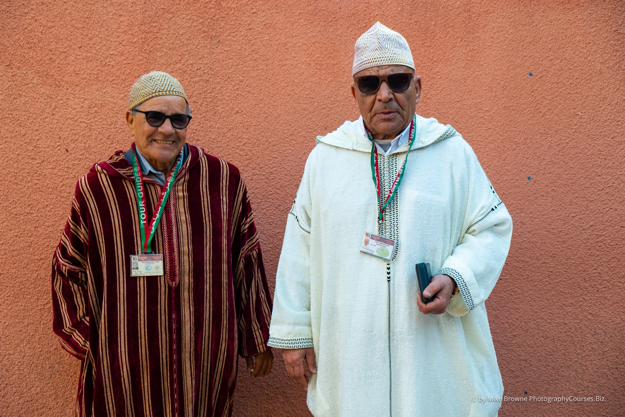two men in North African clothes wearing sunglasses before a pink wall in Marrakesh