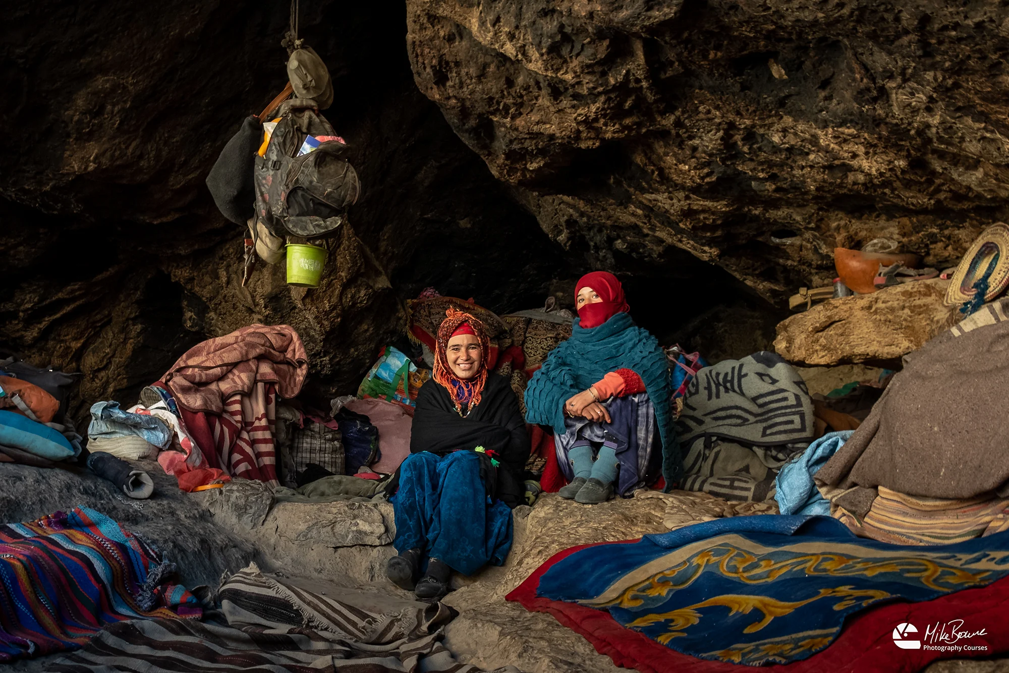 Mother and daughter wearing traditional Moroccan cloths sitting surrounded by their belongings in a cave in Todra Gorge in Morocco