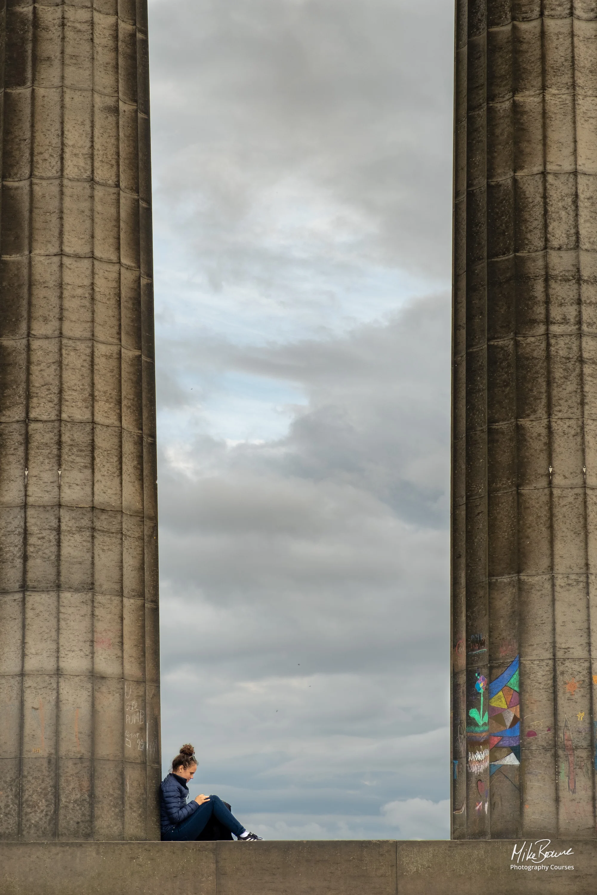 Girl sitting with her back to a pillar reading a book