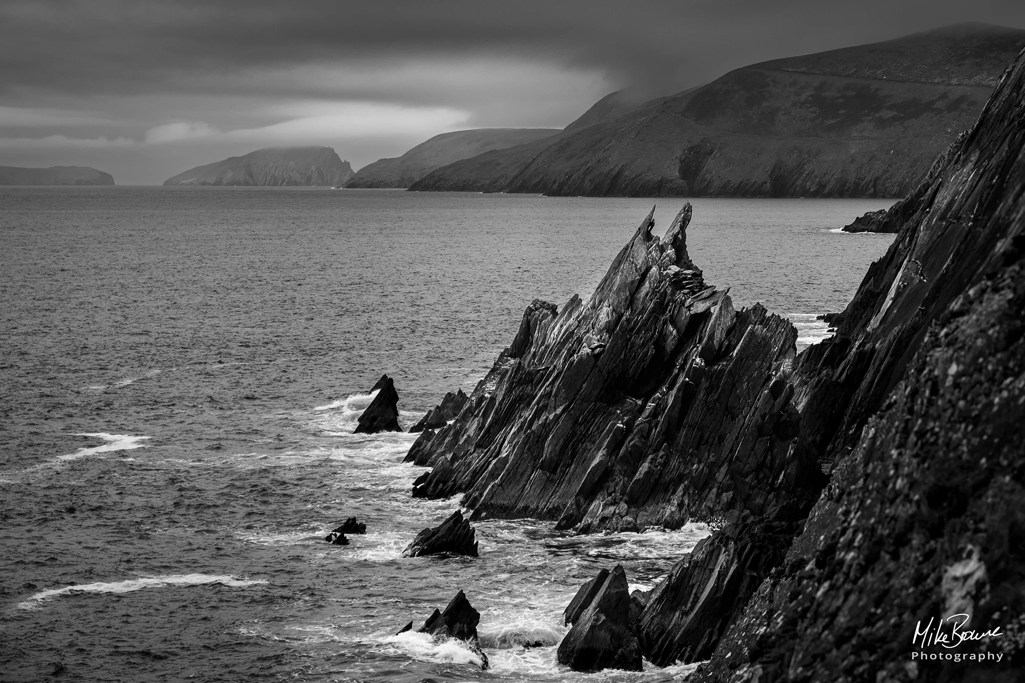 Jagged rocks on a cliff face above the sea and islands in the distance