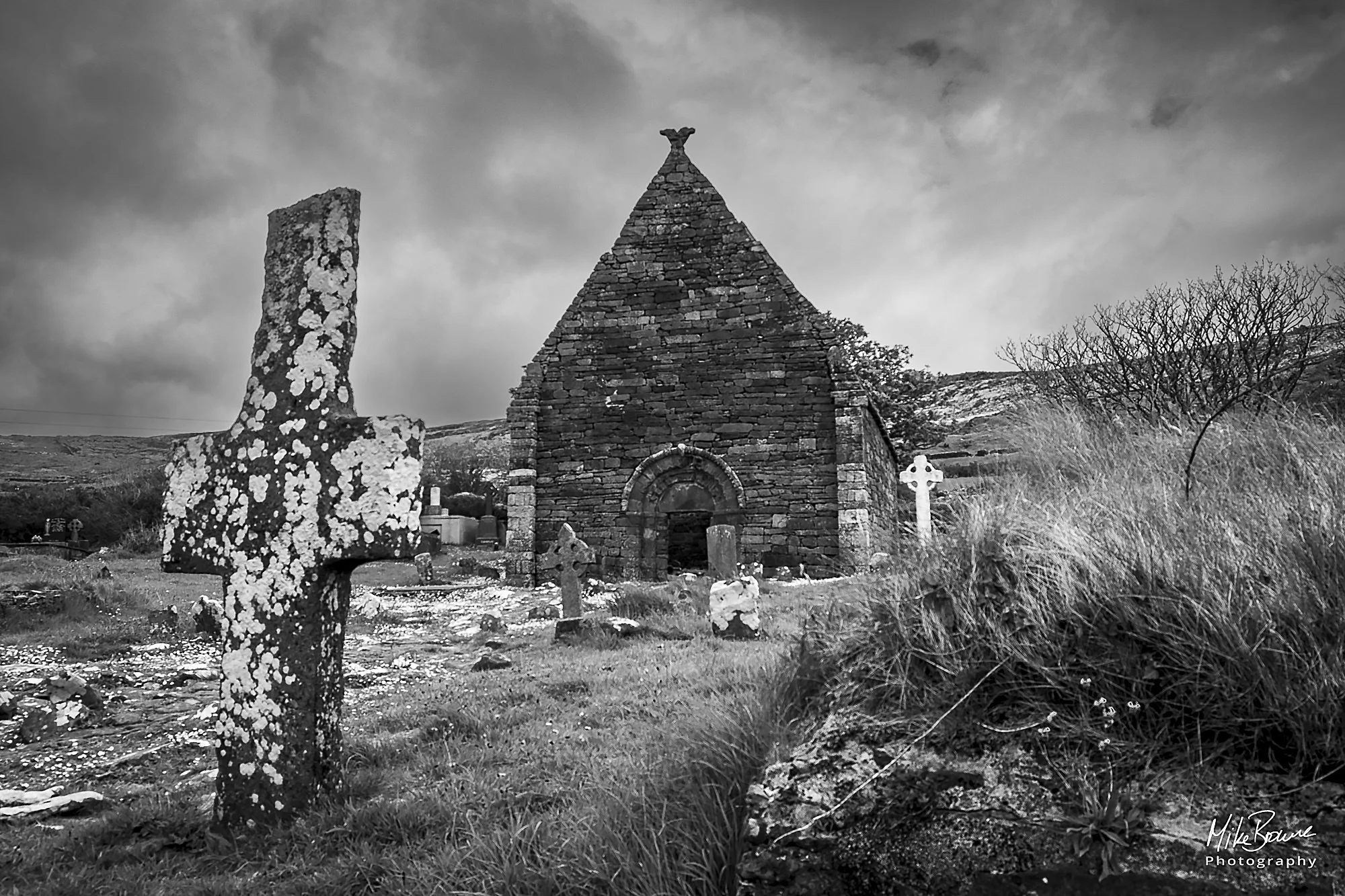 Ancient lichen covered grave stone cross in front of a ruined church near Dingle in Ireland