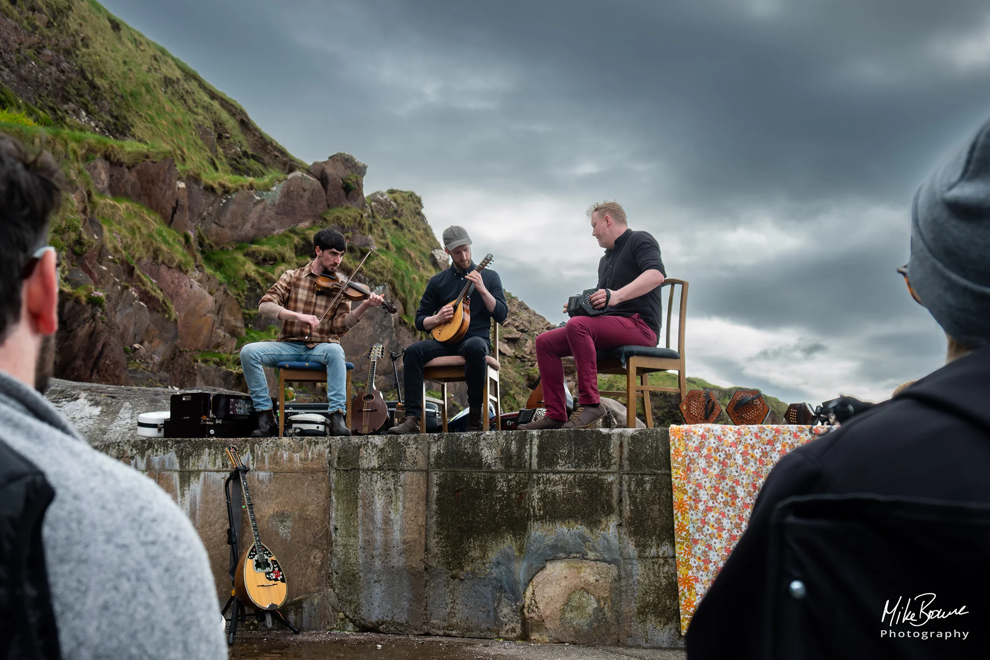 Irish folk musicians Cormac Begley and Ye Vagabonds playing concert on a sea wall with storm clouds above