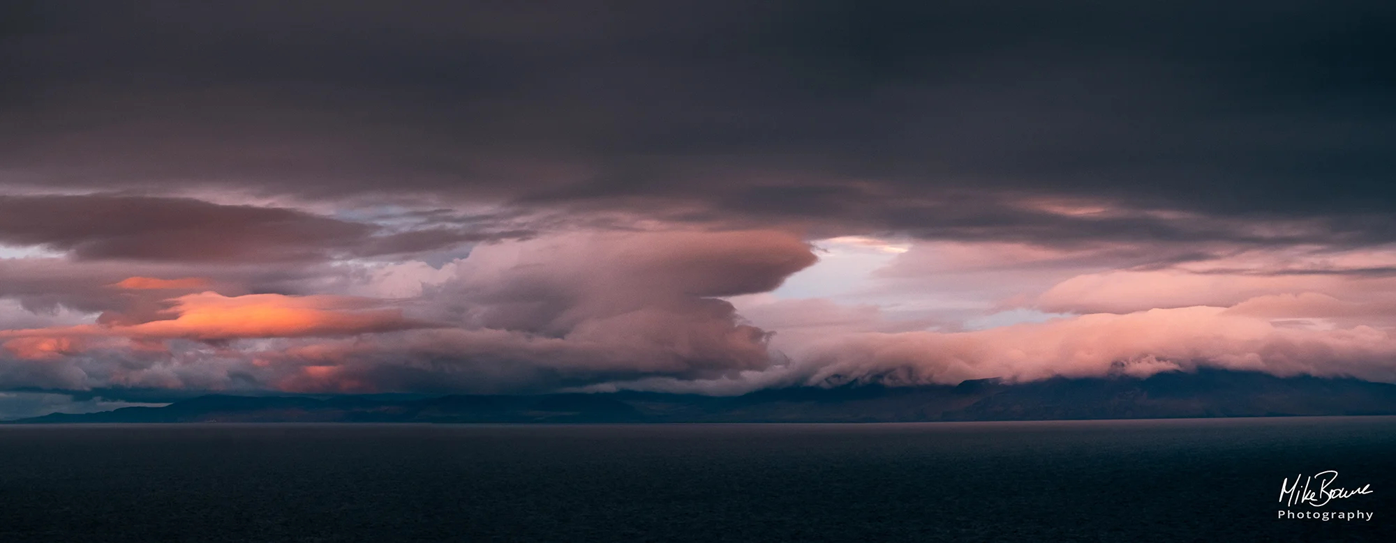 Black storm clouds over the sea with white clouds below glowing red at sunset