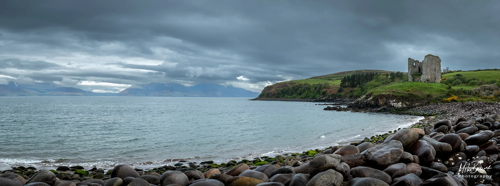 Ruined castle at end of log sweeping rocky sea shore on a cloudy day