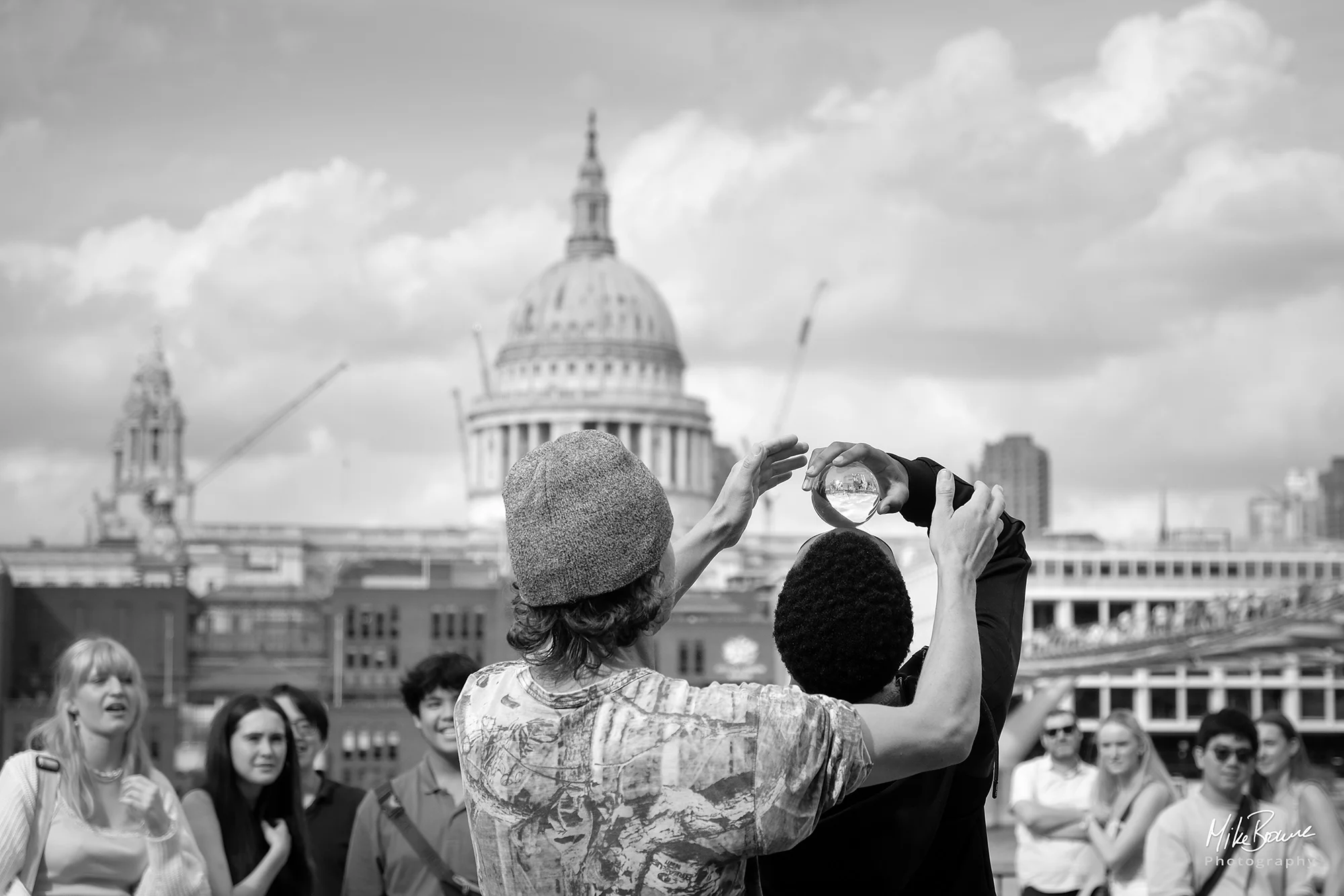 Man balancing crystal ball on another man\'s head with St Pauls Cathedral in Background