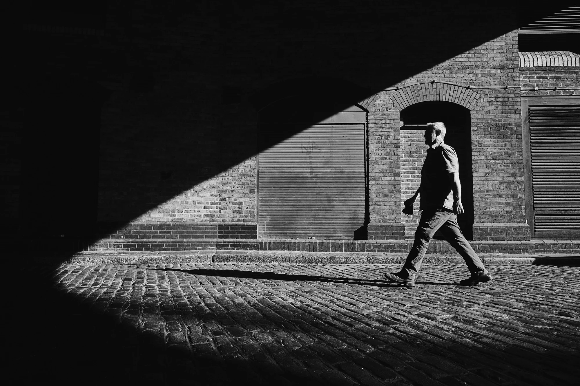 Photographer Mike Browne with camera striding from sunlight into shade on a London street