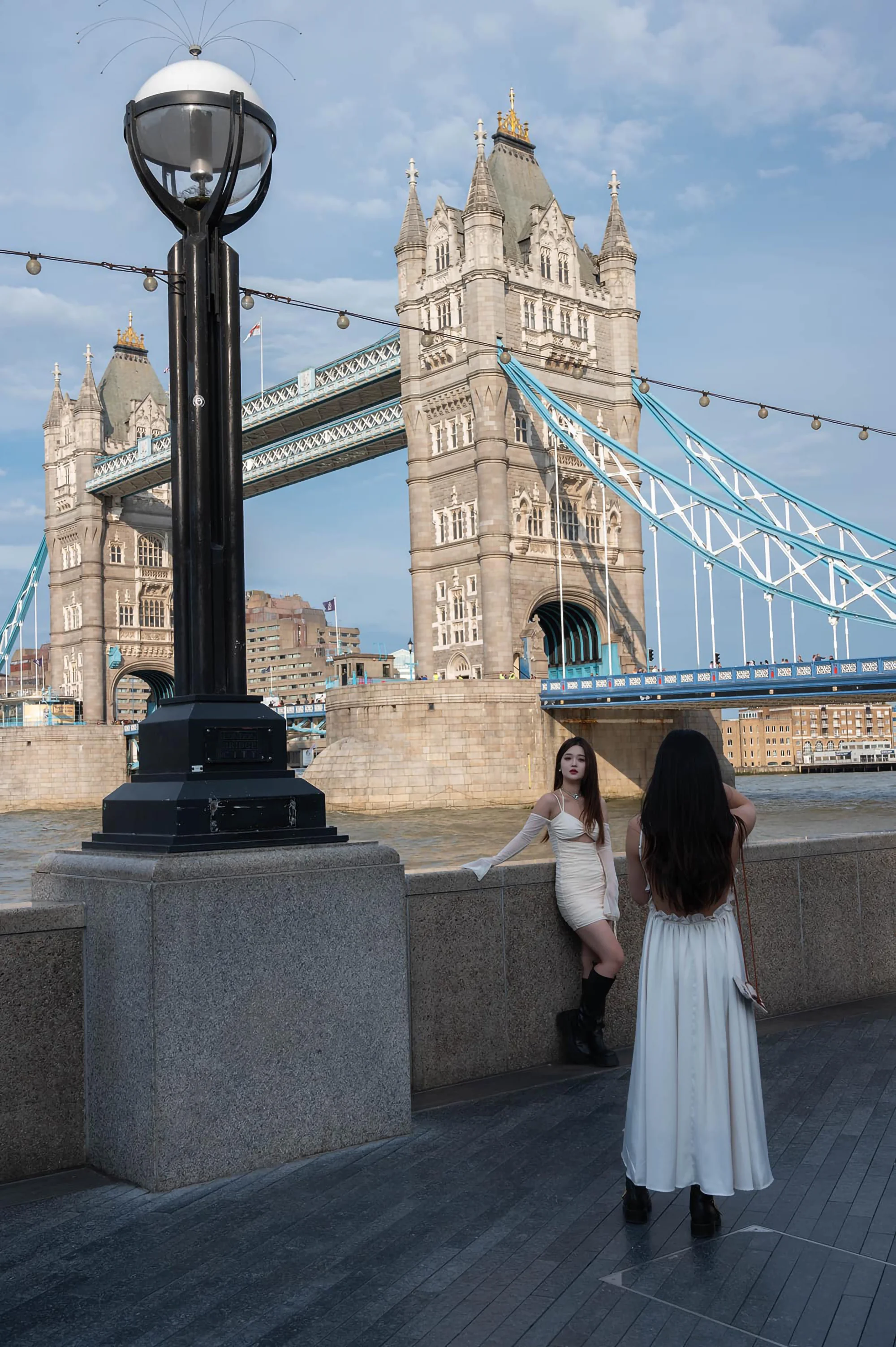 Two young Asian women influencers in white dresses pose for photos with Tower Bridge in background