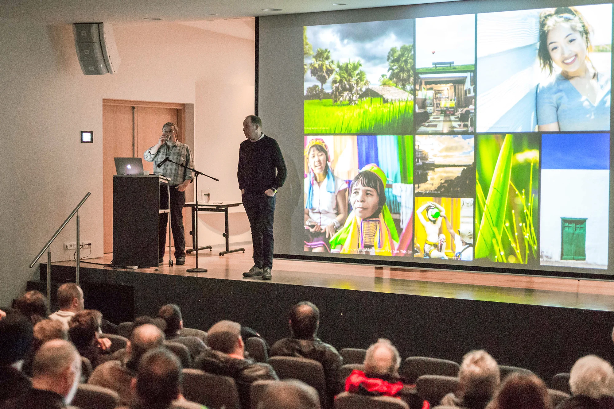 Mike Browne and MC on stage with big screen of photos in front of a large audience