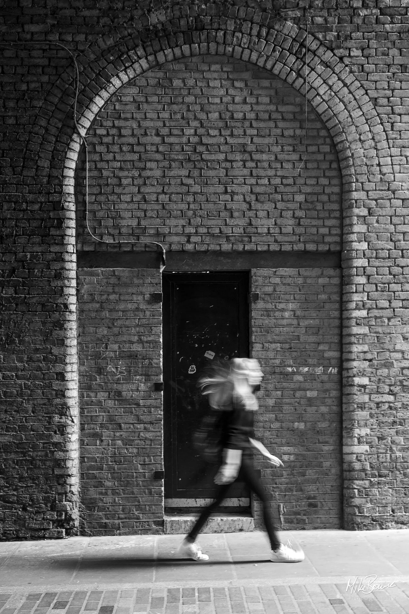 Tall ornate brick arched door way with girl walking in front toward the right