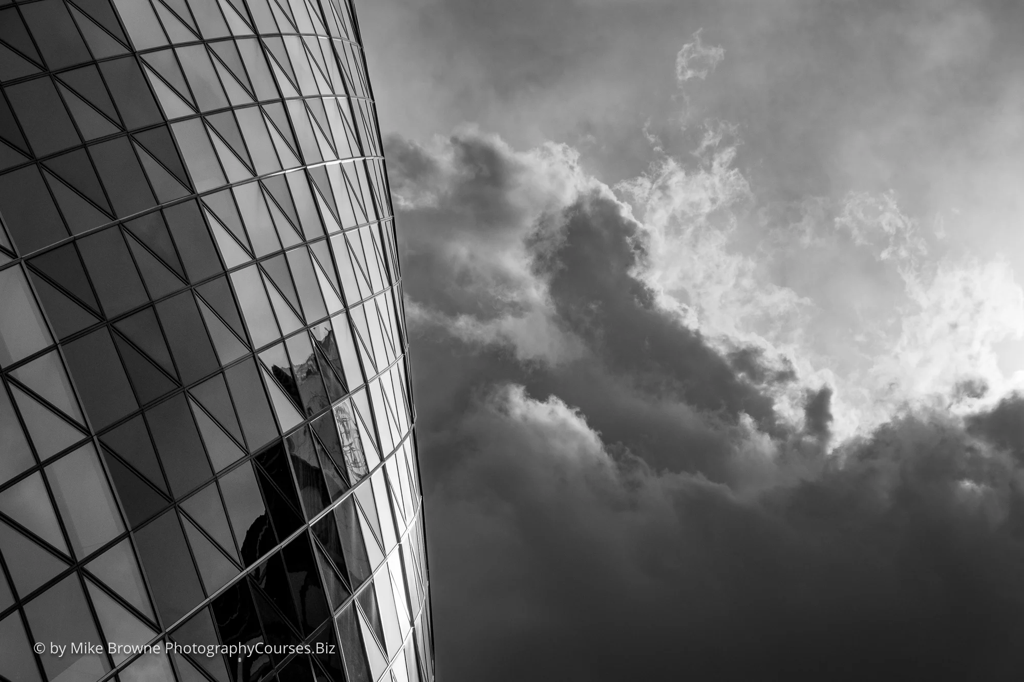 Multitude of glass triangles making up the gherkin with cumulus clouds covering the sun