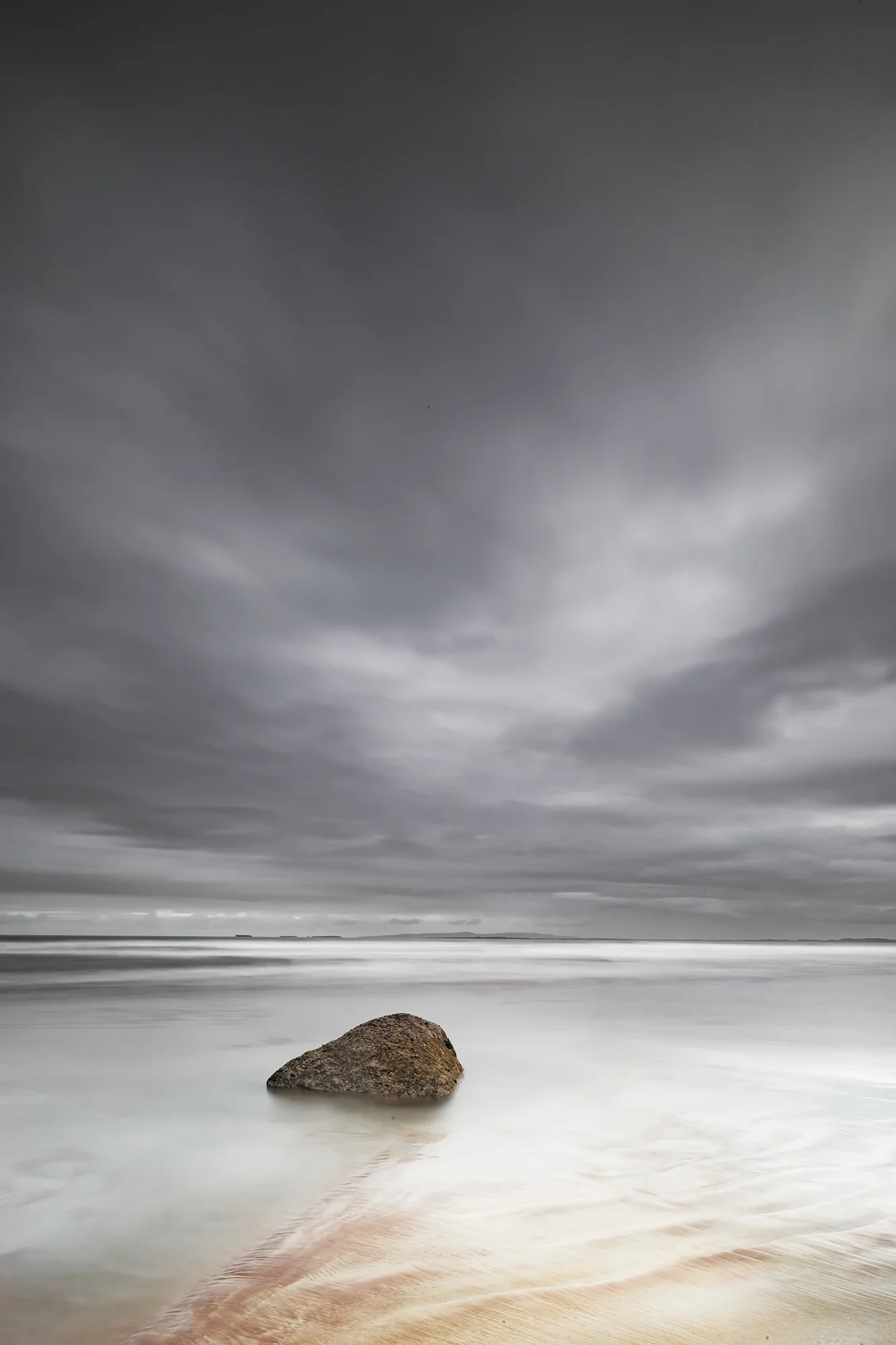 Single rock in calm sea at Fermoyle Beach with reflection of sunrise