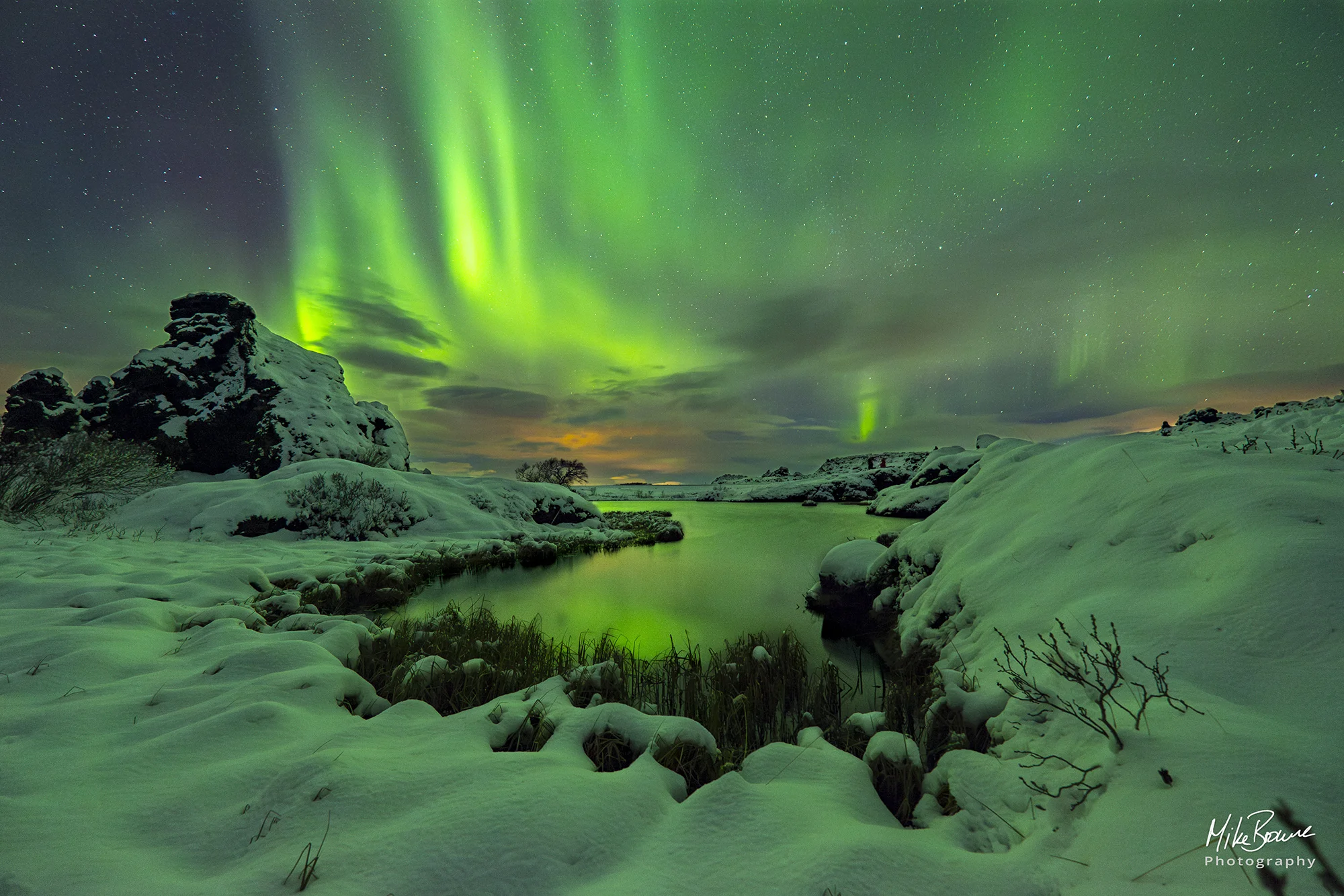 Green Aurora Borealis in sky above a pool of water surrounded by snow