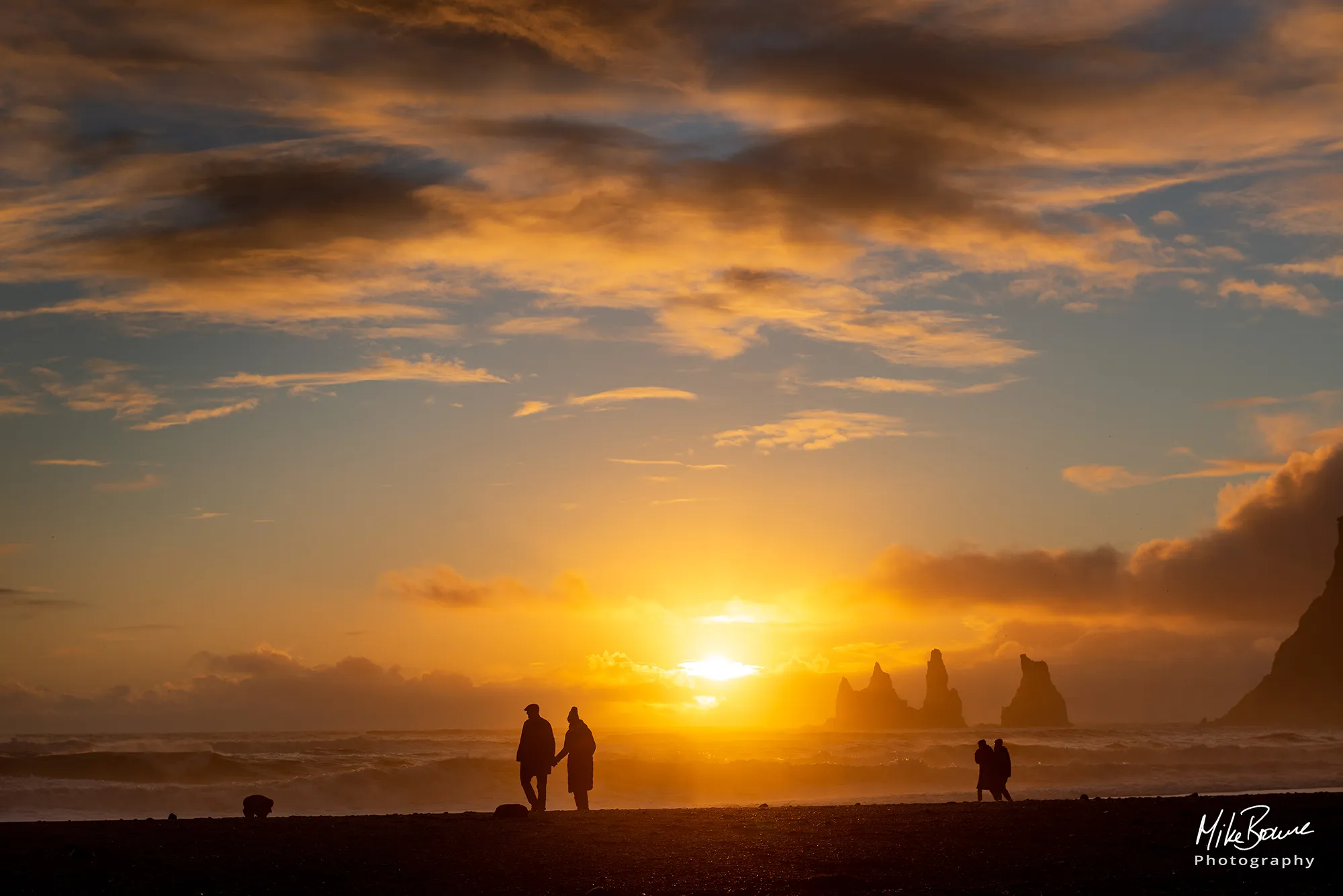Silhouettes of two couples walking on beach at sunset in Vik Iceland