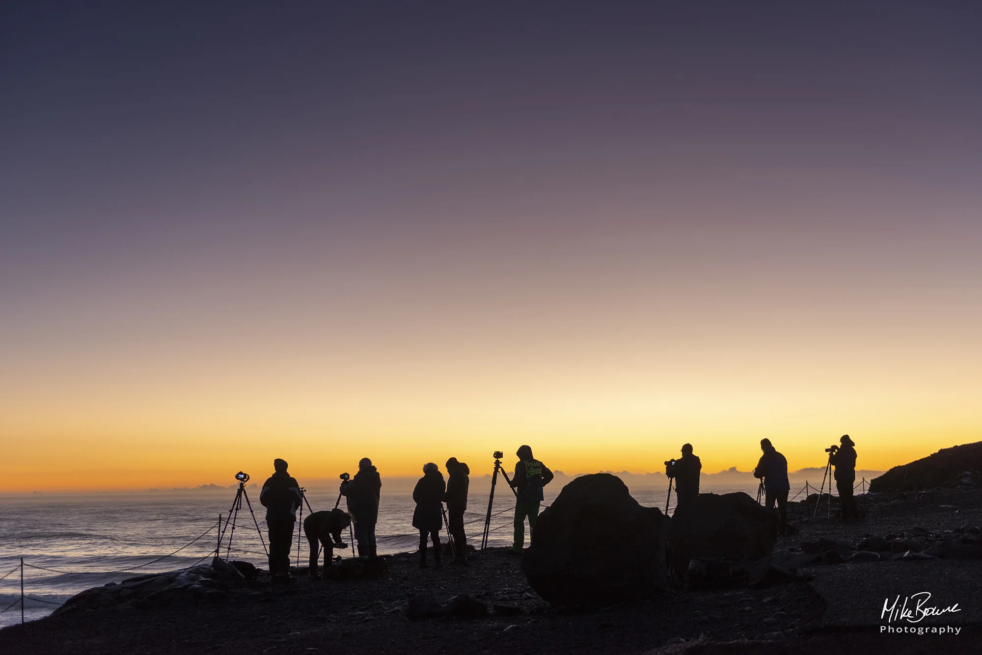 Group of photographers and tripods photographing sunrise over ocean at Reynisdrangar Iceland