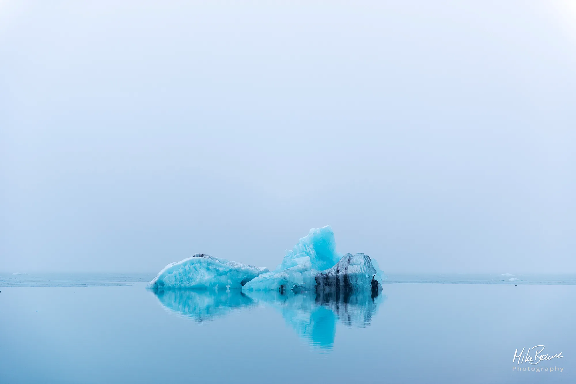 Iceberg and reflection floating on still blue water