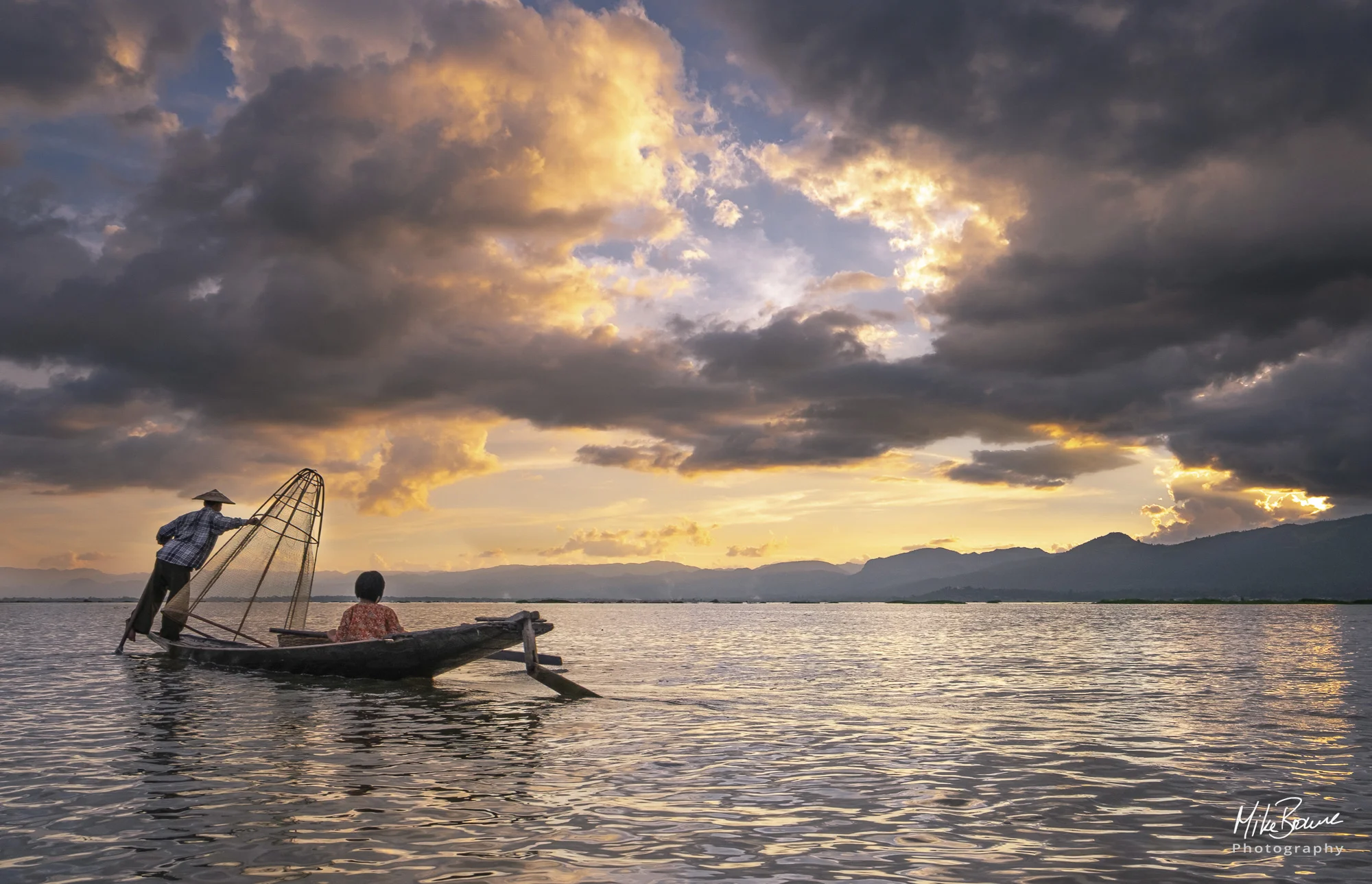 Fisherman and girl child watch sunset from small boat on Inle Lake