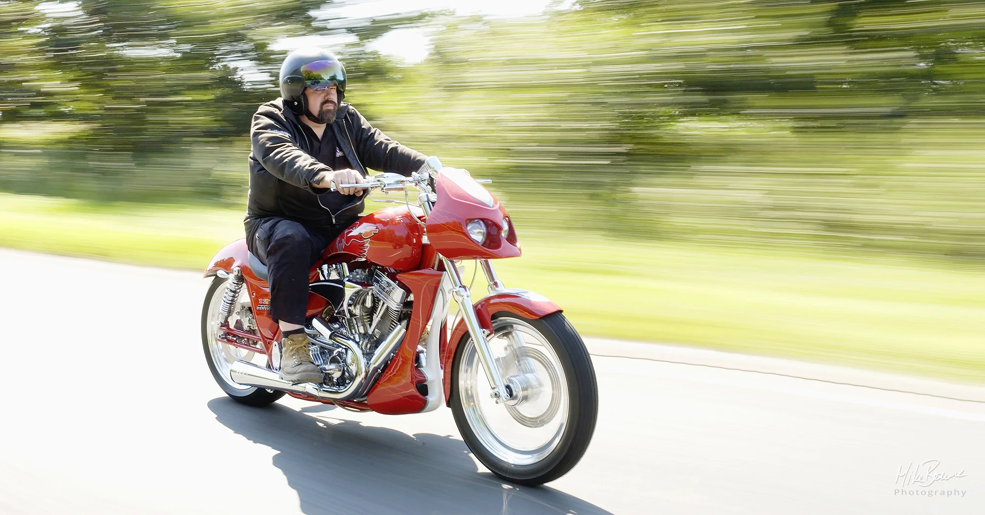 Man wearing black clothes riding a red Harley Davidson custom motorcycle