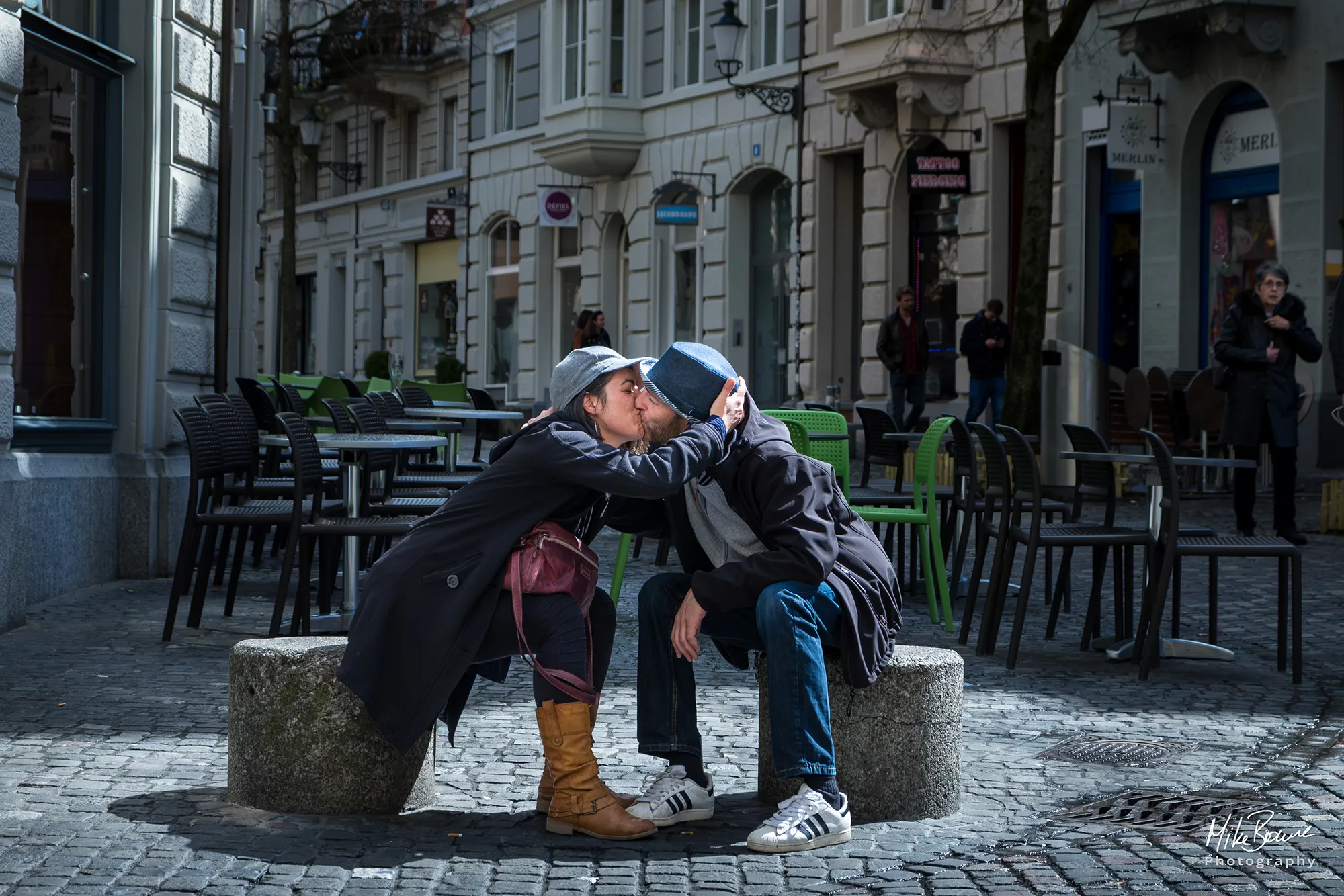 Woman and man wearing hats kissing in pool of sunshine in Zurich