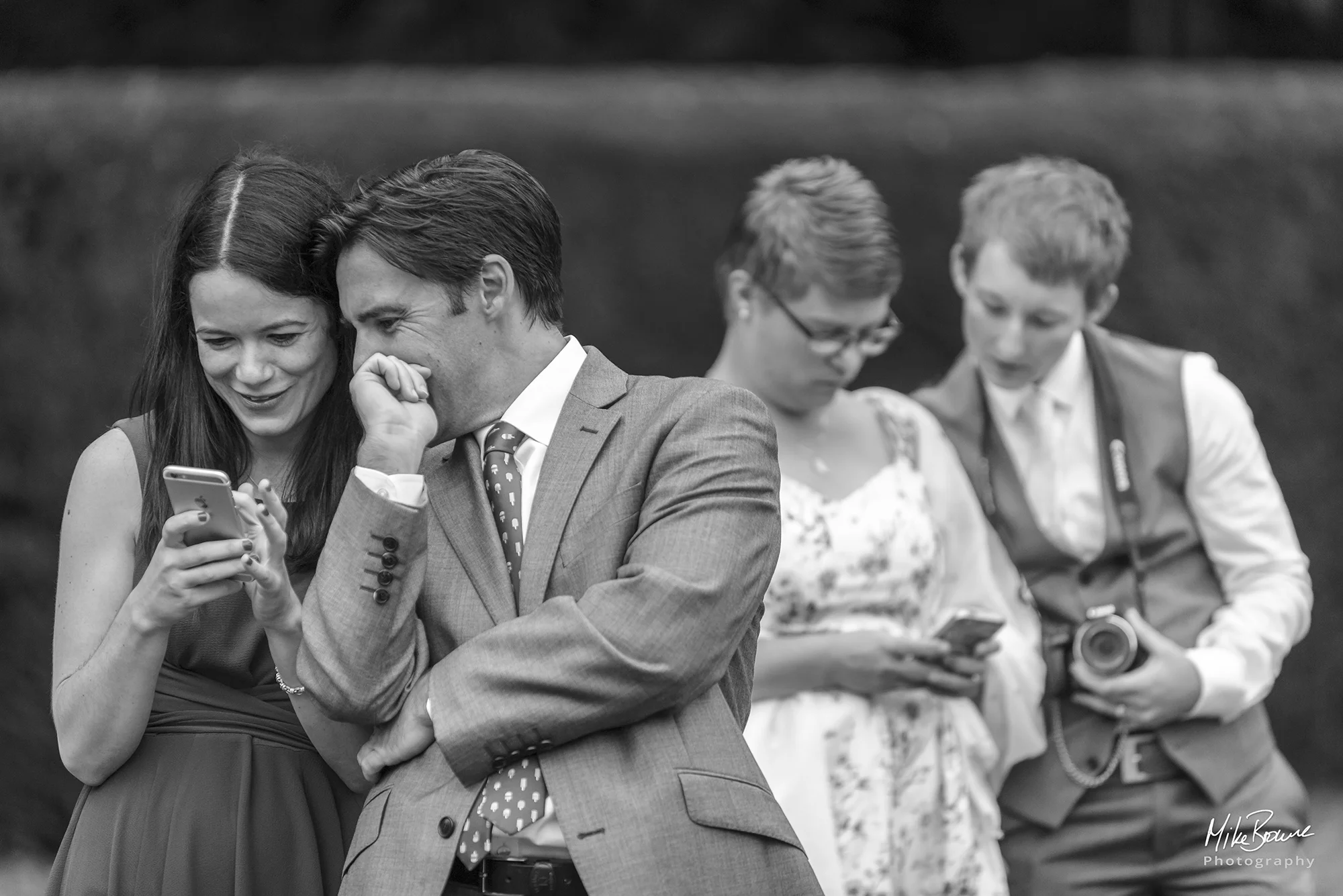 Two couples looking at their phoned at a wedding