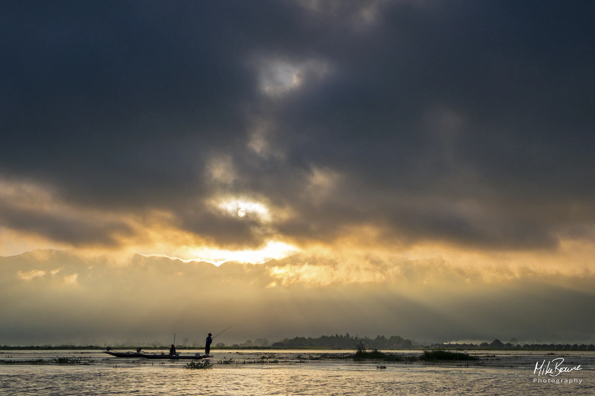 Two fishermen in small boat on Inle Lake, Myanmar and heavy storm clouds approaching from behind