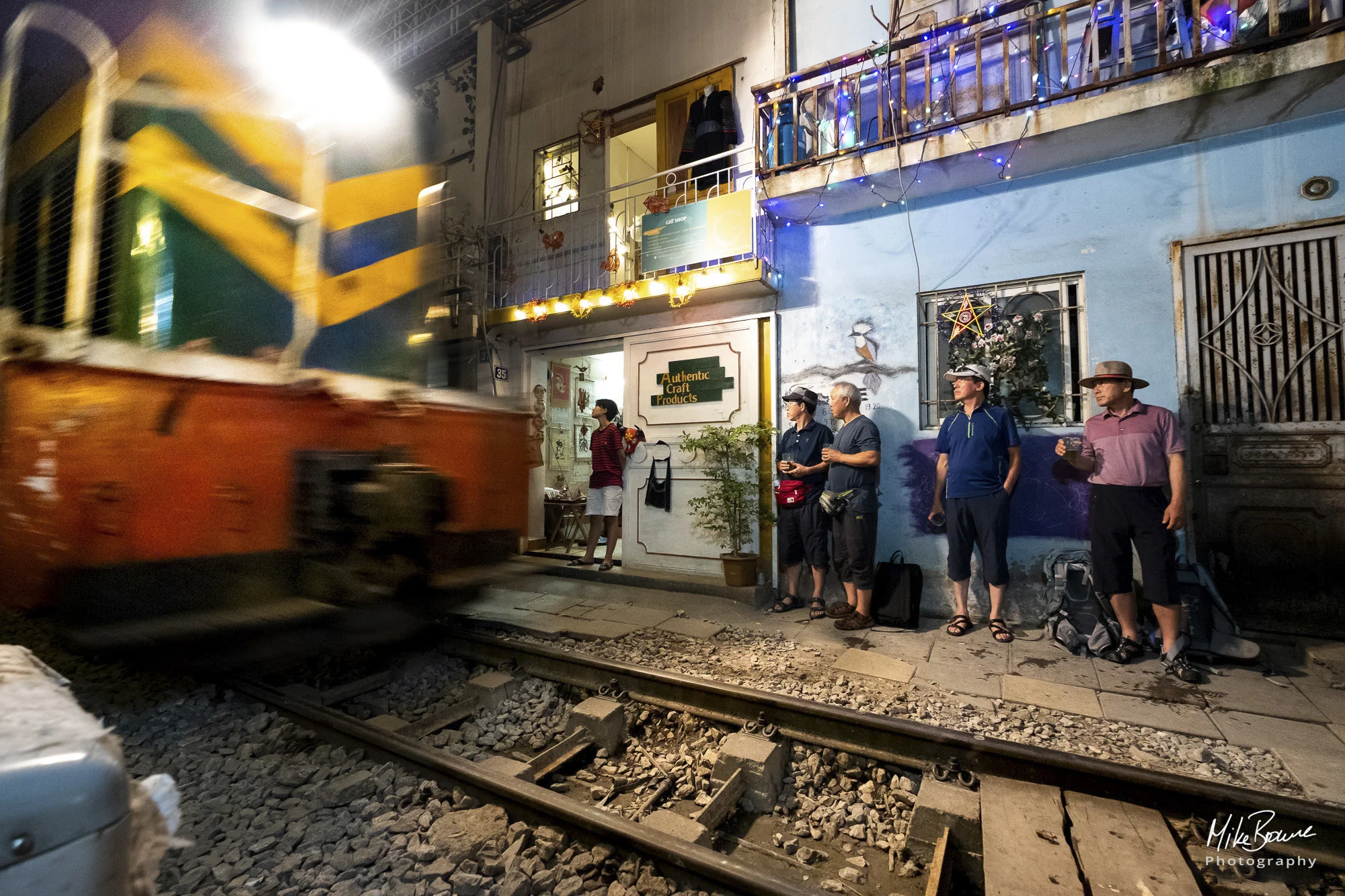 Men stand back against wall as diesel train comes by in Train street, Hanoi, Vietnam