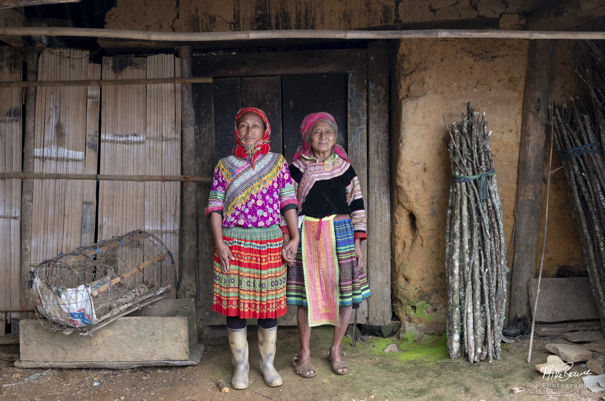 Hmong Mother and daughter, chicken cage and bundle of wood by front door of a house in Hoàng Su Phì, Vietnam